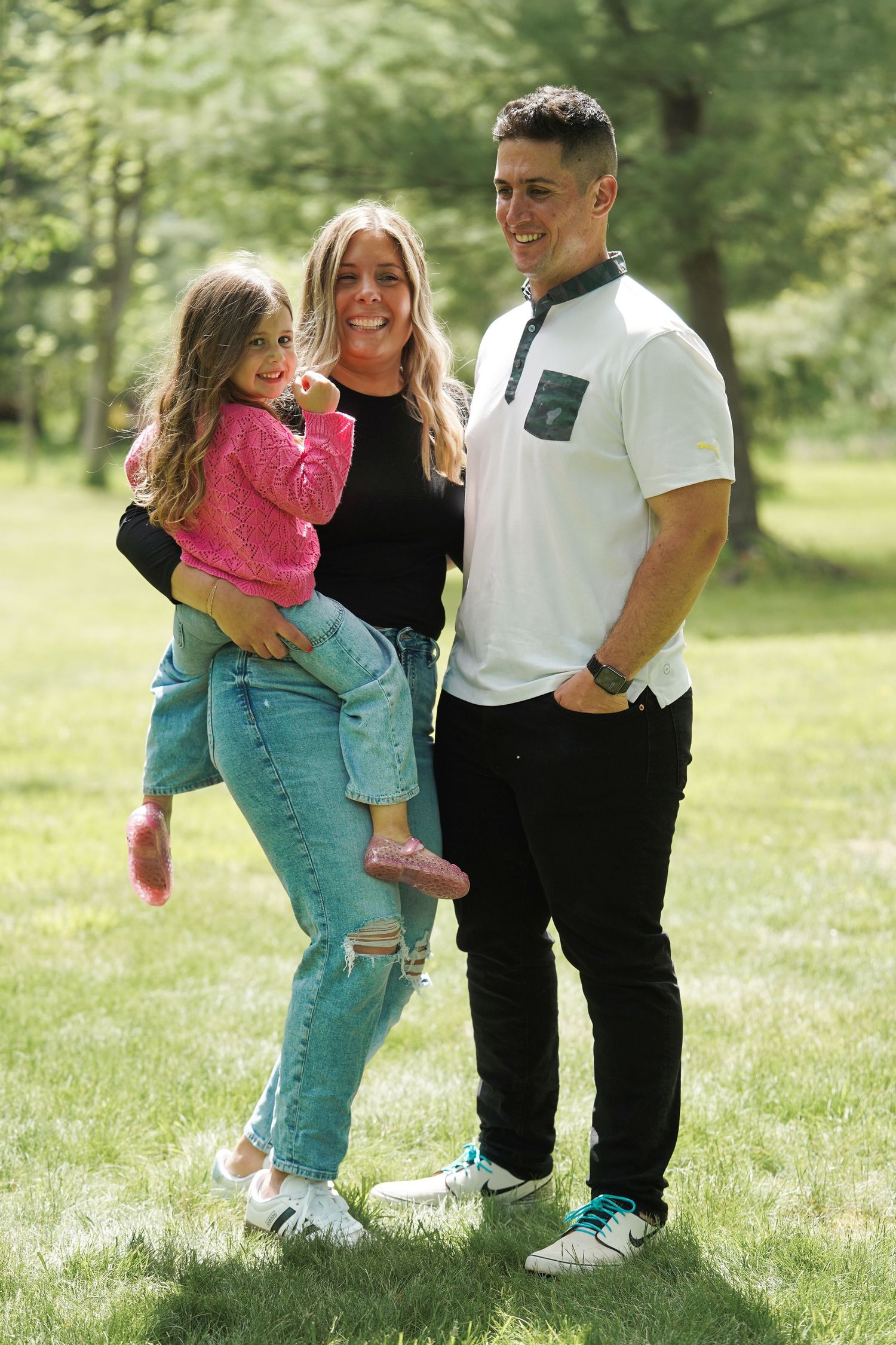A family spending time together outdoors in a grassy park on a sunny day wearing casual clothing.