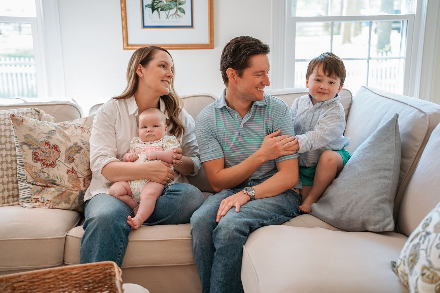 Family members sitting close together on comfortable sofa in sunlit home interior.