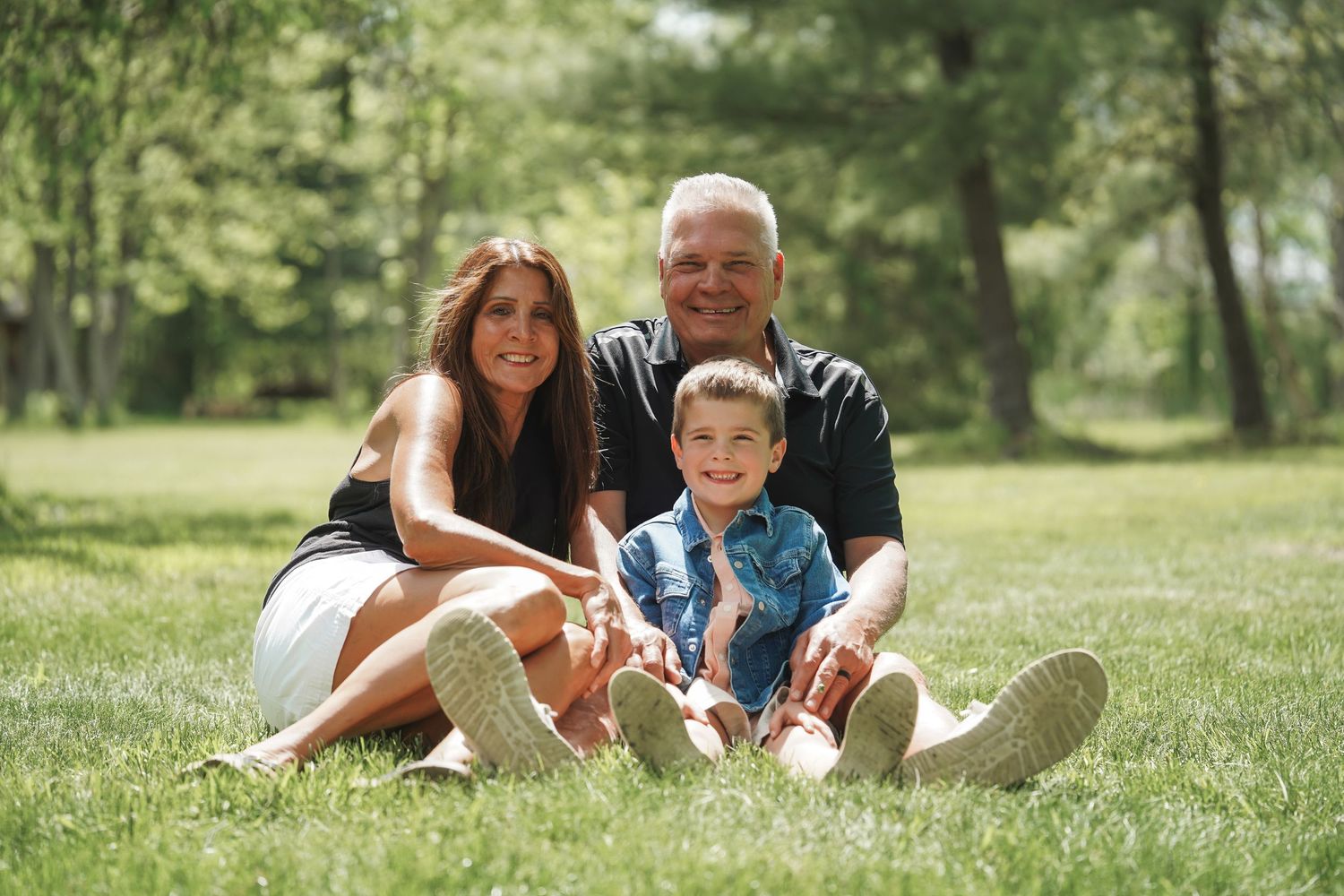 Three people sitting together on green grass in a sunny park on a beautiful summer day.