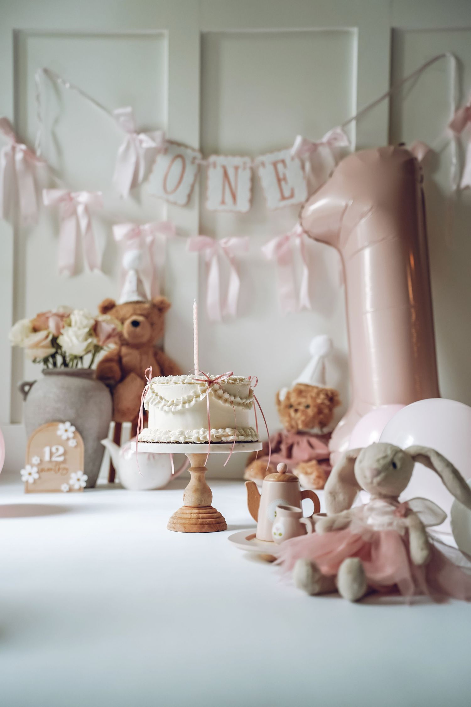 Soft pink nursery decor featuring stuffed animals, banners, and pastel accessories arranged in a delicate vignette.