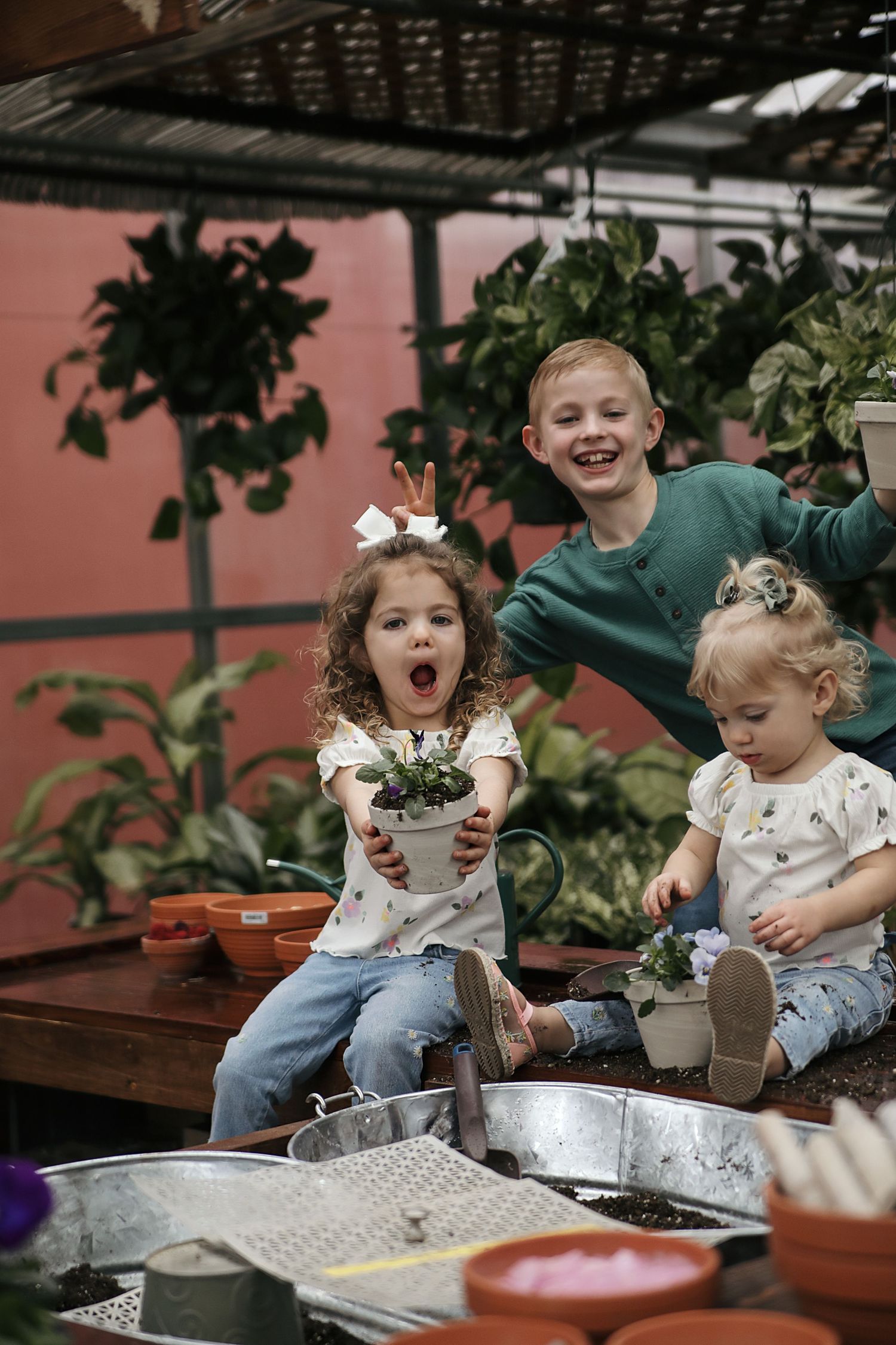 Multiple images showing young children engaged in gardening activities with soil and potted plants in a greenhouse setting.