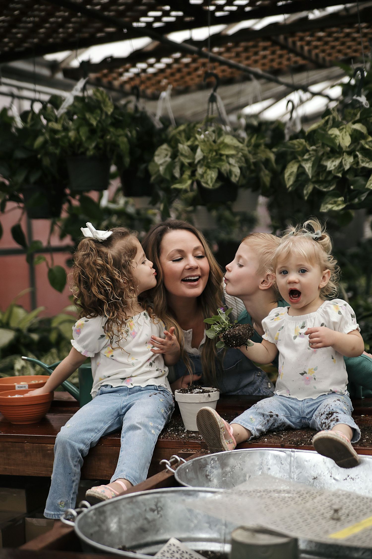 A joyful moment shared between family members sitting together in a greenhouse garden with hanging plants.