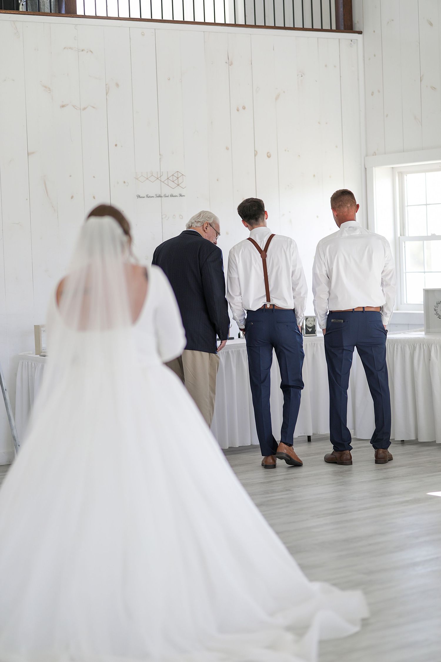 A bride in a flowing white gown stands behind a group of formally dressed people facing away.