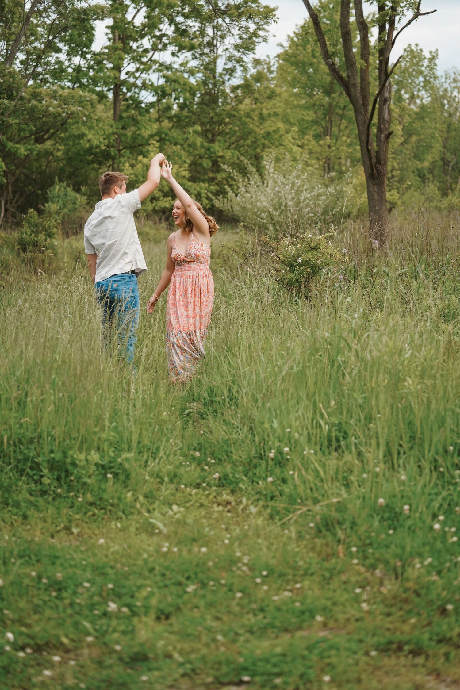 Couple walks together through a peaceful meadow of tall grass and wildflowers on a sunny spring day.