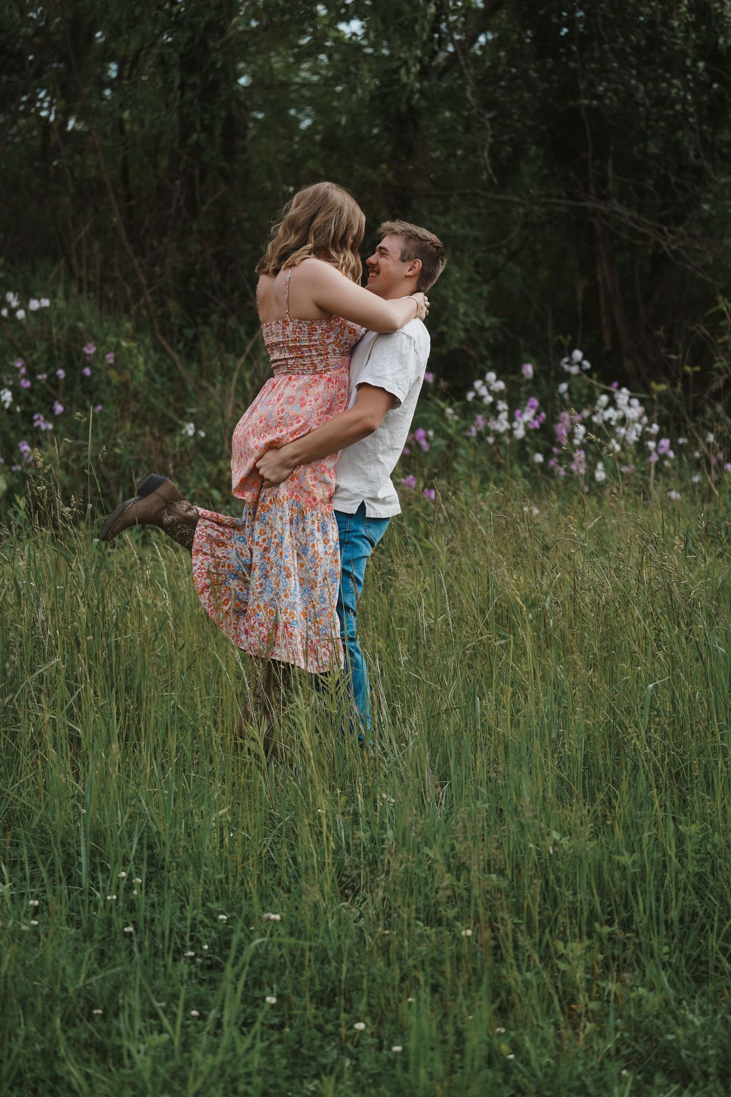 A romantic embrace in a wildflower meadow with tall grass and trees in the background at dusk.