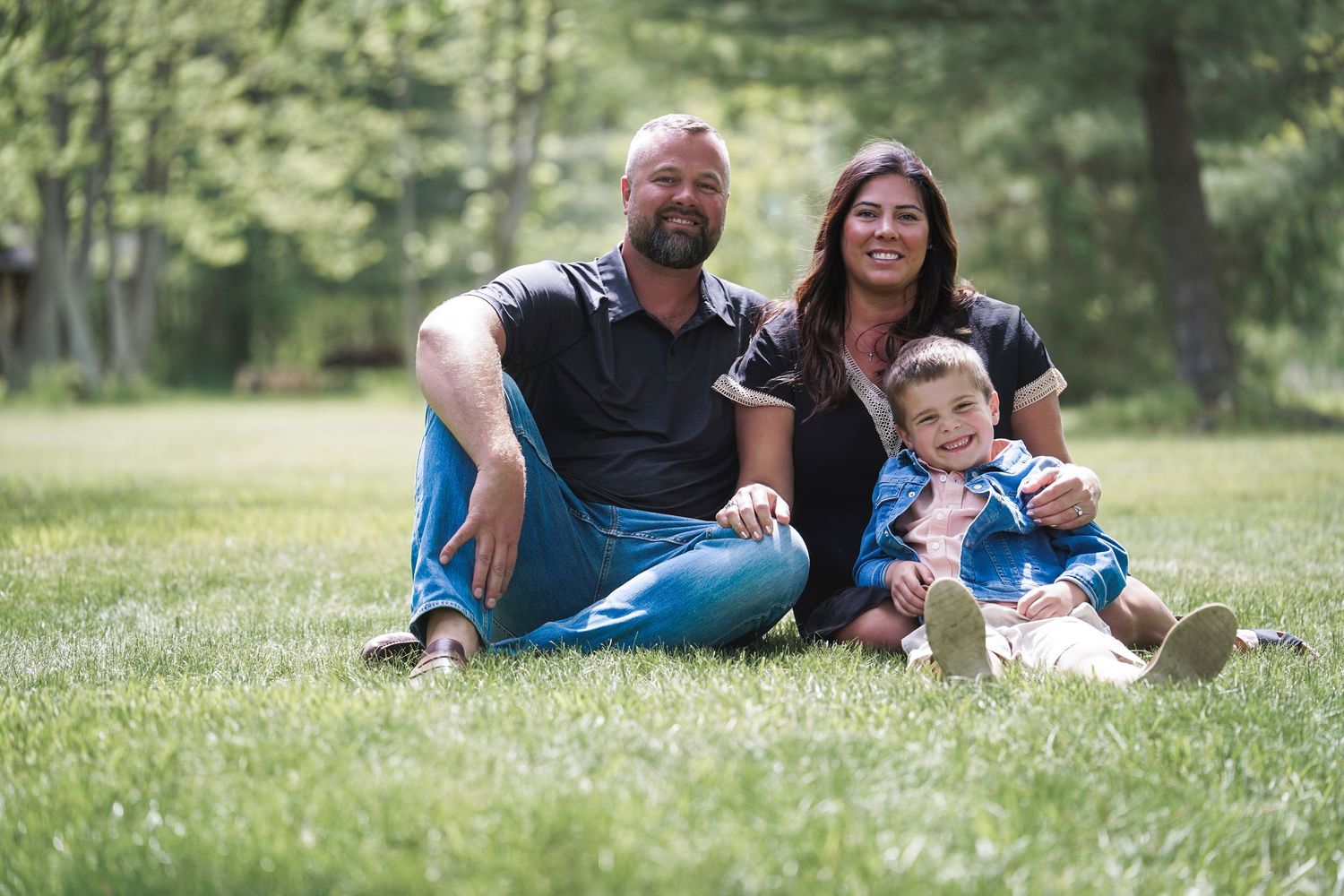 Family group laying in grassy field outdoors during summer photoshoot.