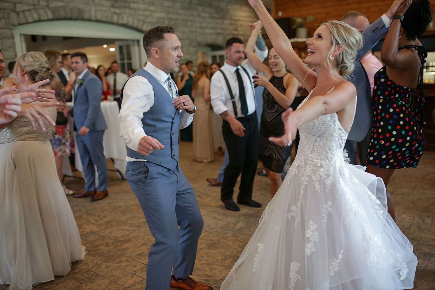 Lively dancing and celebration at a wedding reception in a rustic brick-walled venue.