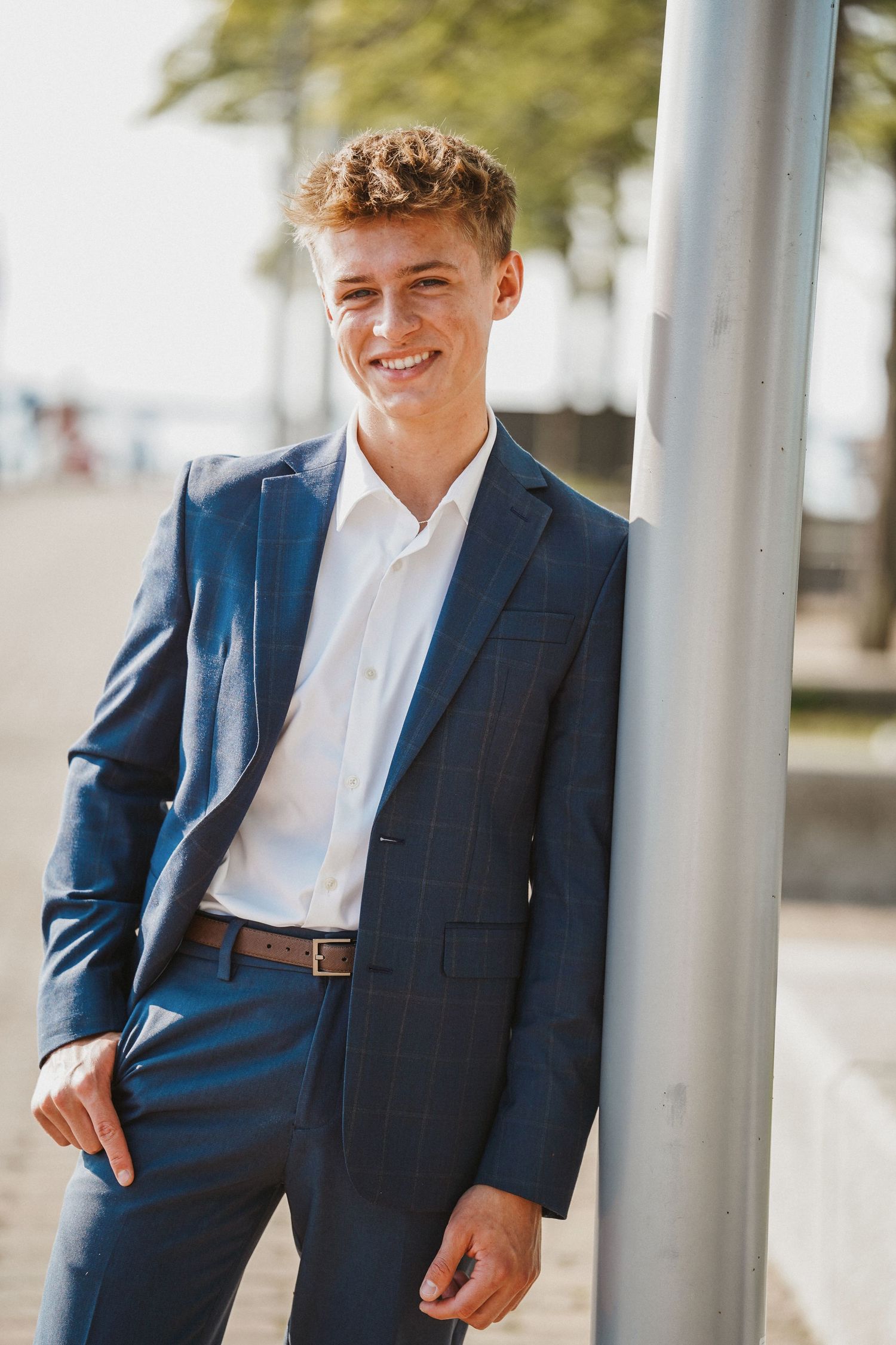 Professional portrait of a man in a navy blue suit and white dress shirt standing against light-colored columns.