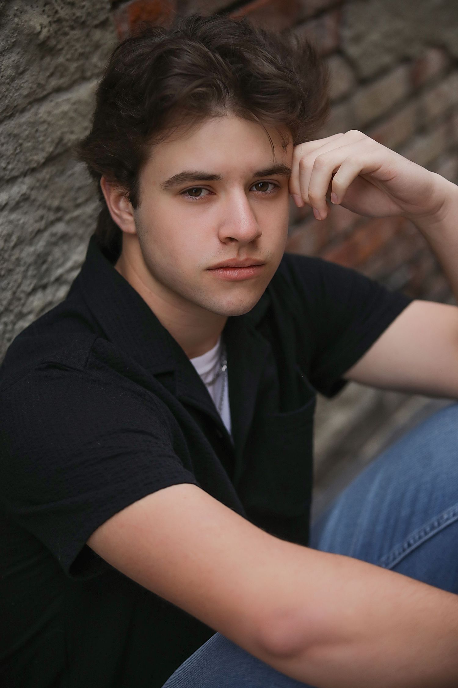 A series of moody portrait photographs showing someone in a black suit jacket against a textured stone wall background.