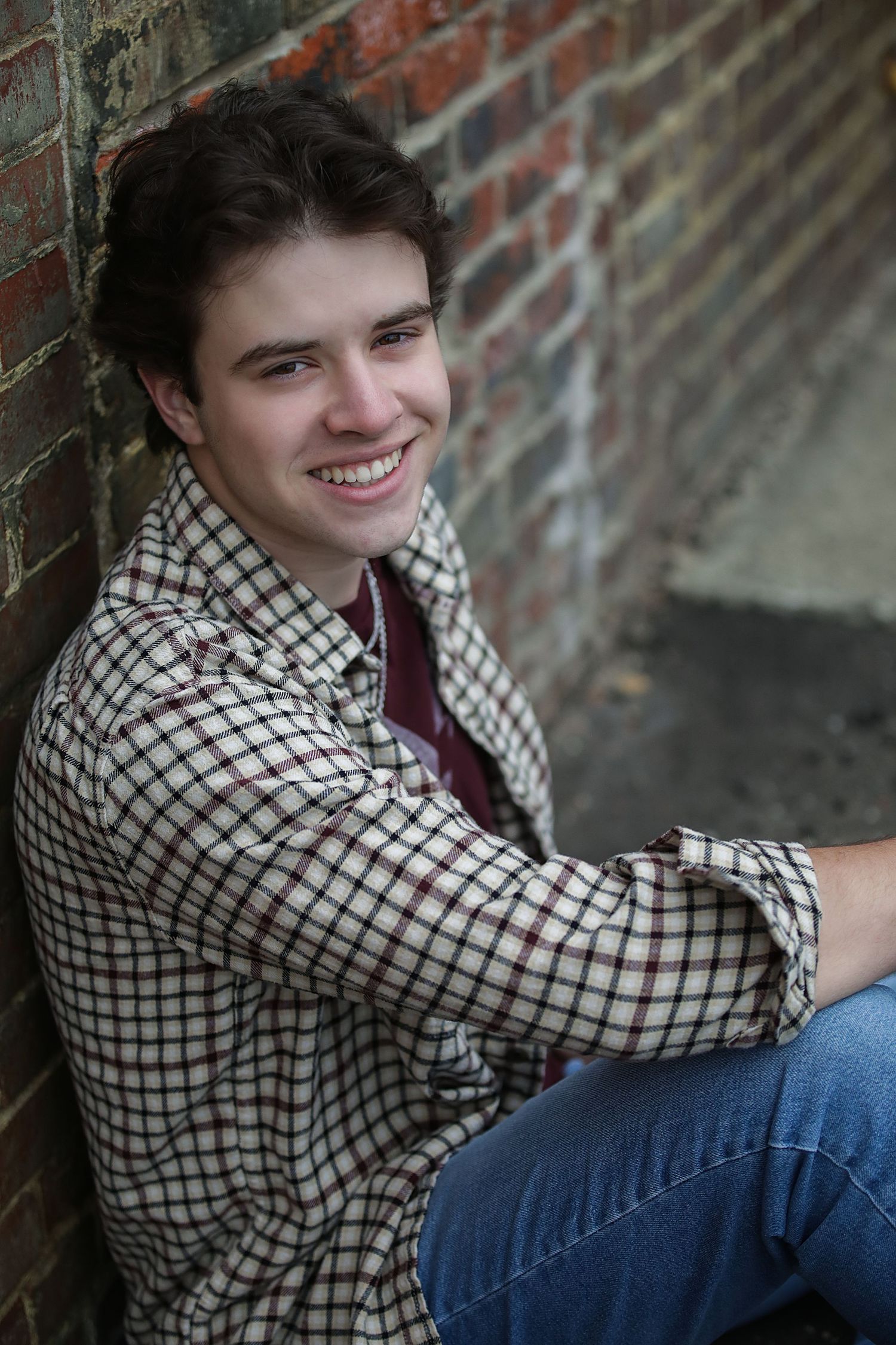 A person wearing a checkered shirt and jeans poses casually against a brick wall in a series of similar shots.