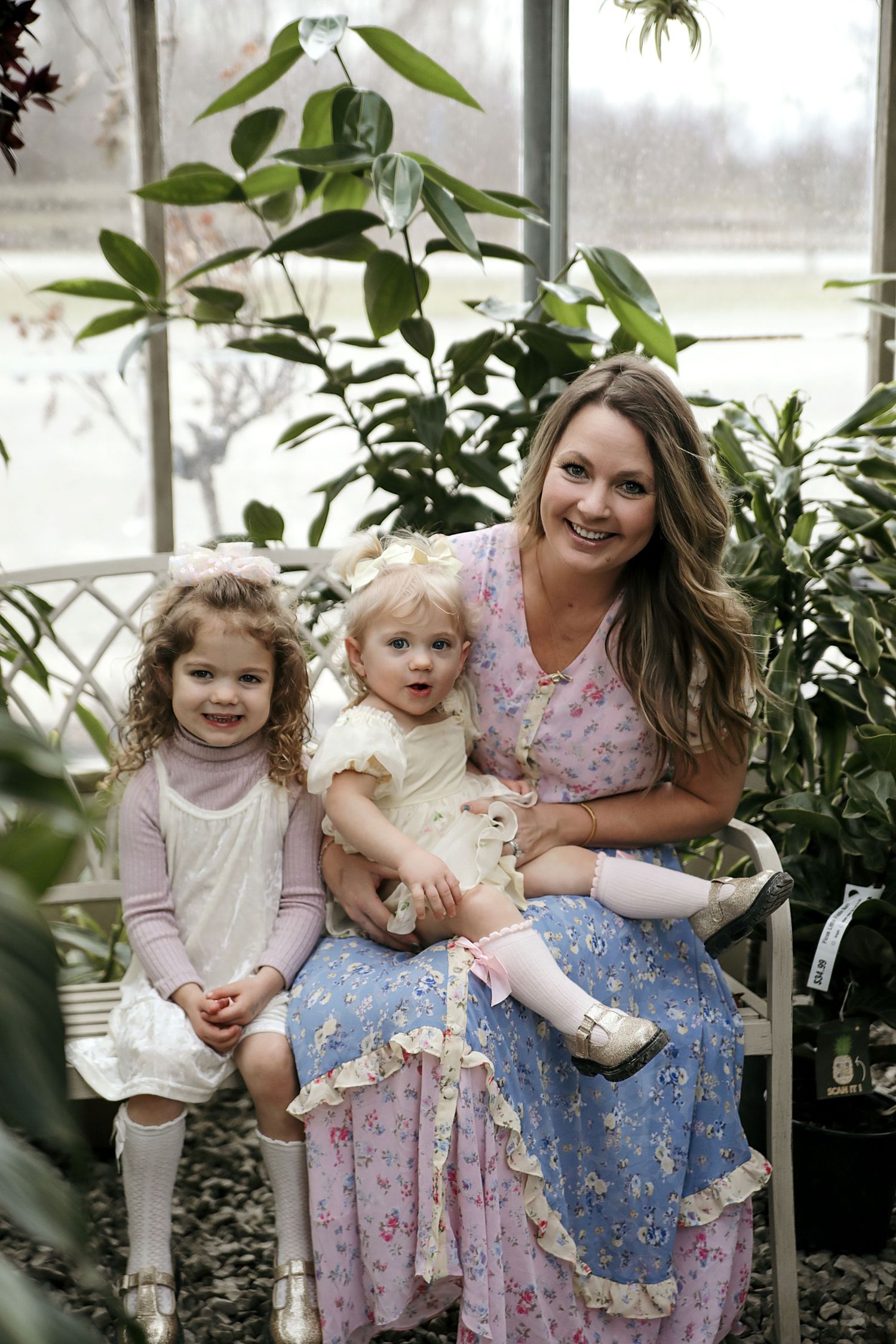 A greenhouse scene with family sitting together surrounded by lush greenery and plants in soft natural lighting.