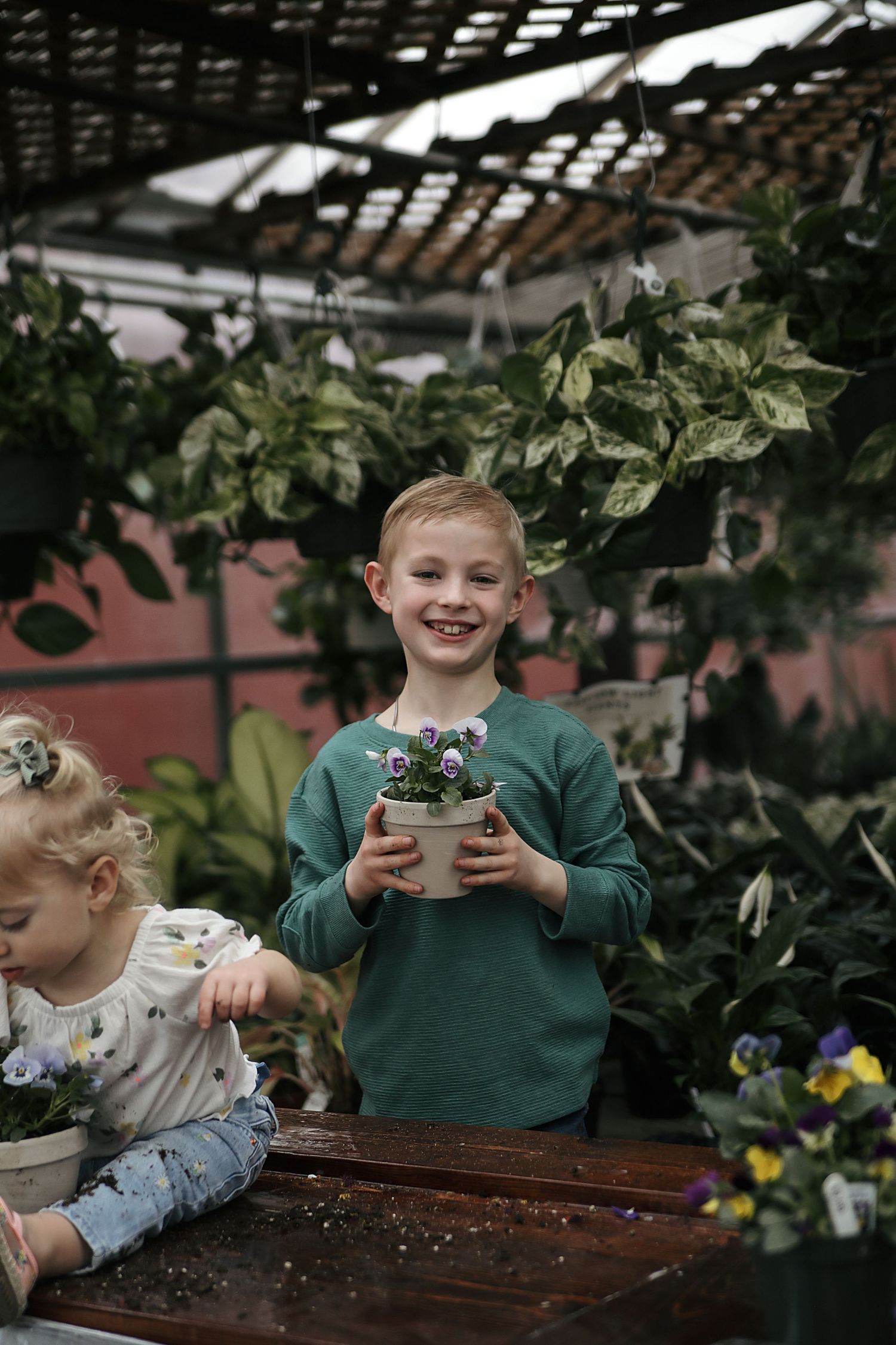 Two young gardeners having fun while planting flowers together in a greenhouse.