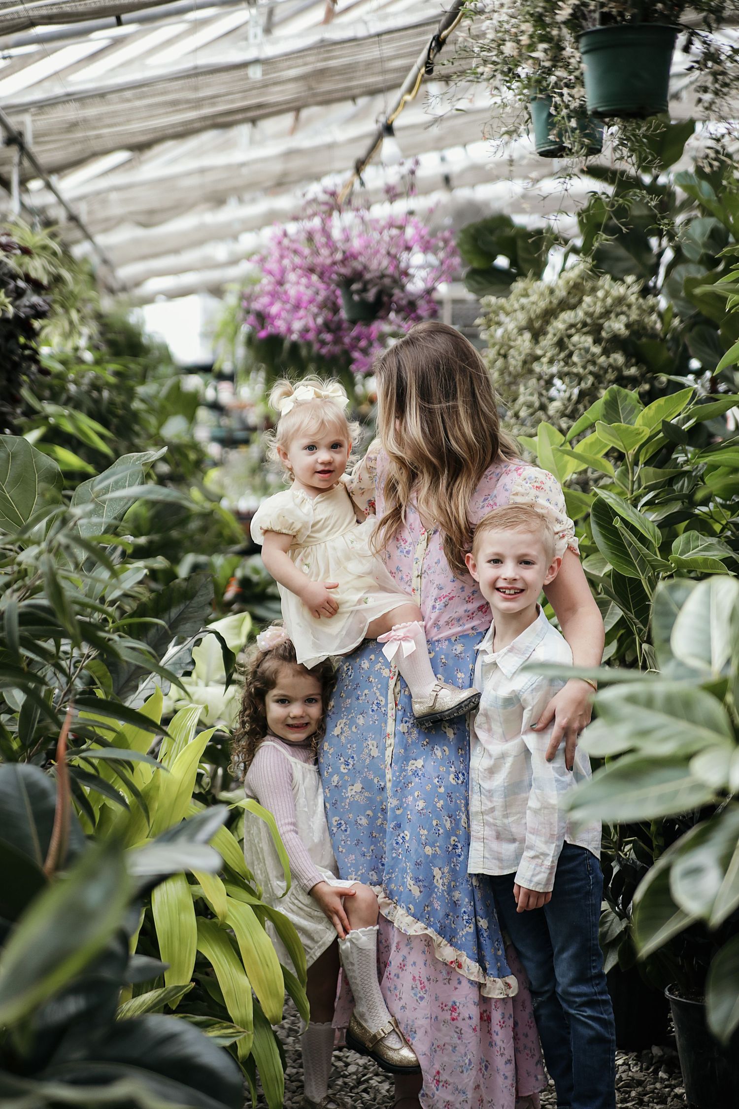 Children play and explore together in a greenhouse filled with lush tropical plants and blooming flowers.