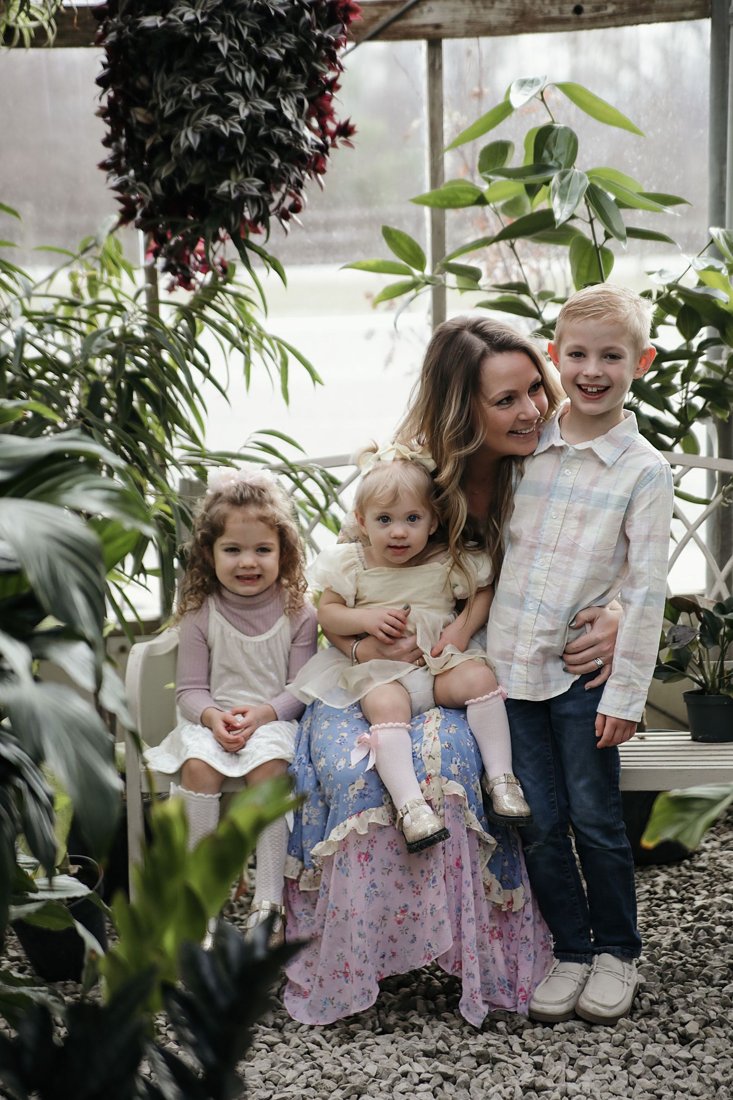 A family poses together in a greenhouse surrounded by lush tropical plants and greenery.