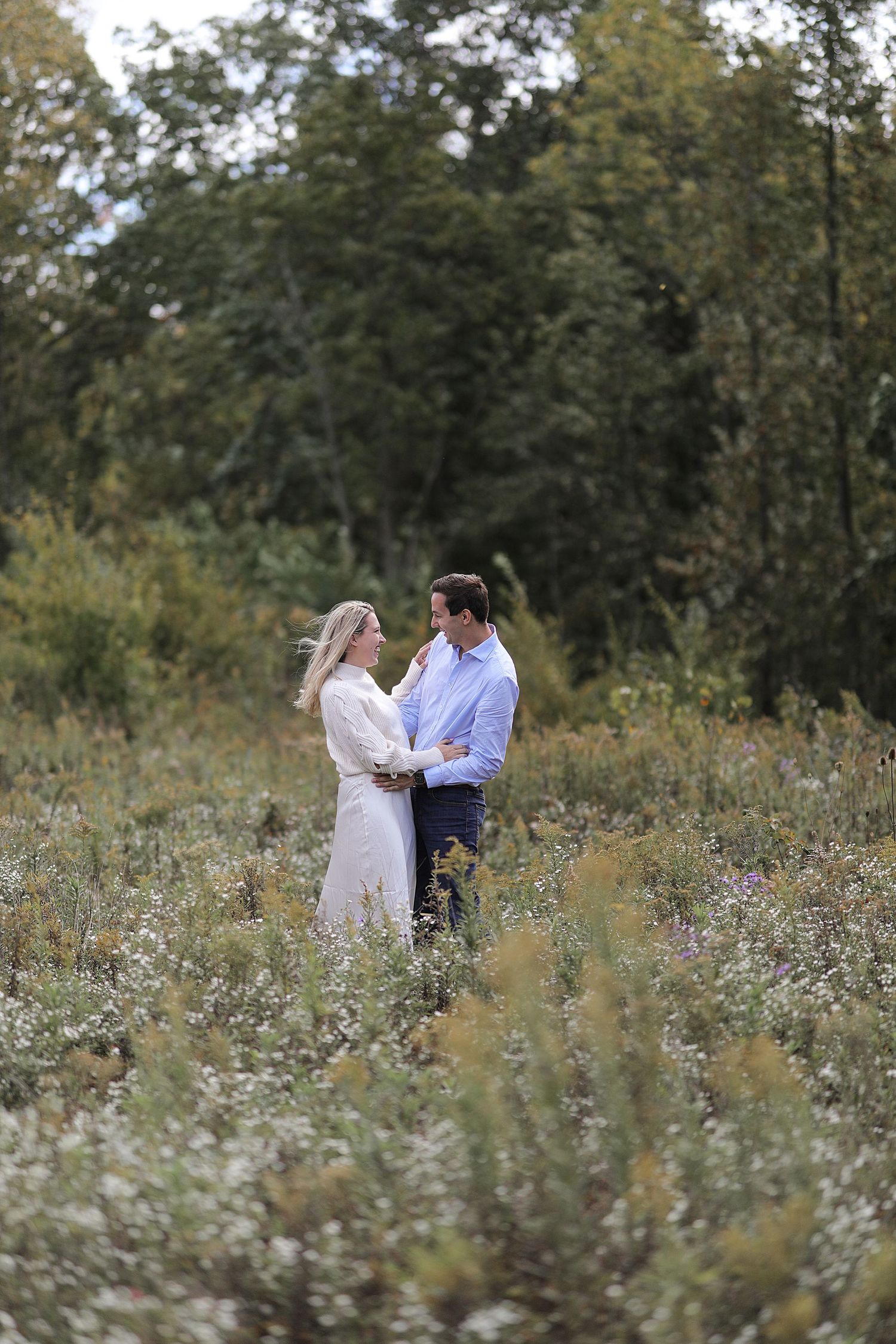 A romantic couple stands together in a wildflower meadow on a late summer afternoon.