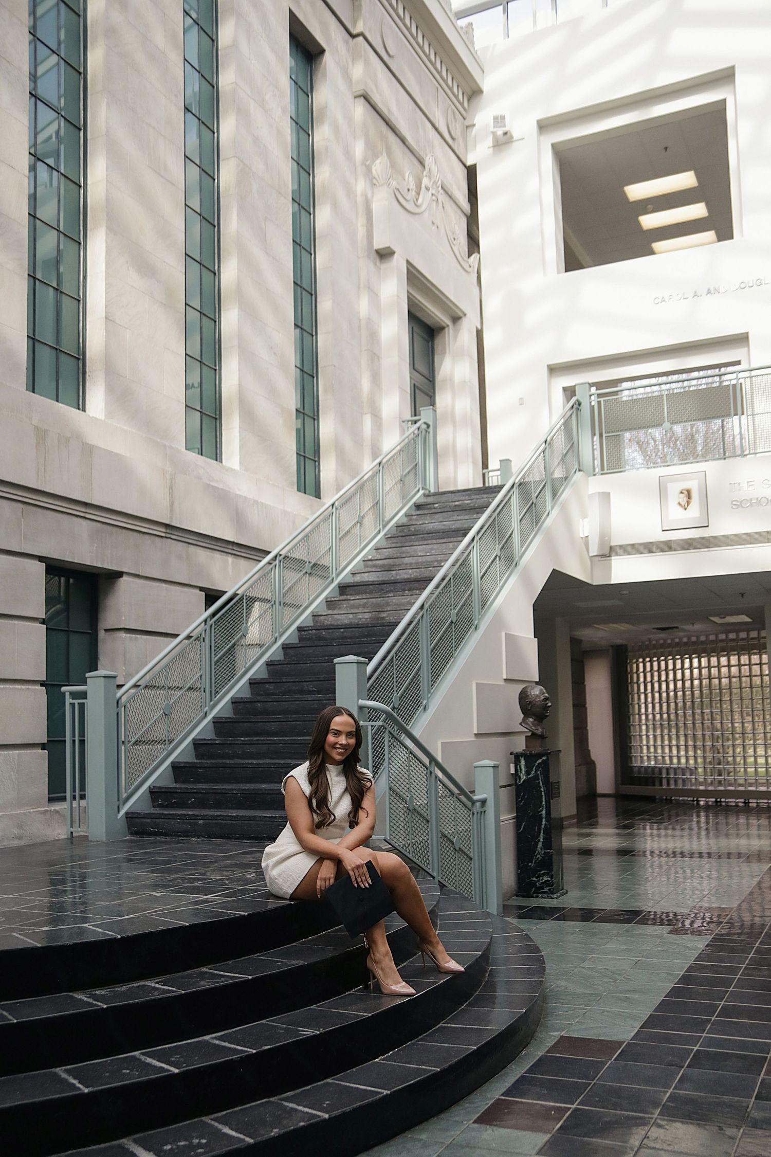 Modern architectural interior with glass railings and dark tiled steps featuring a person in casual attire.