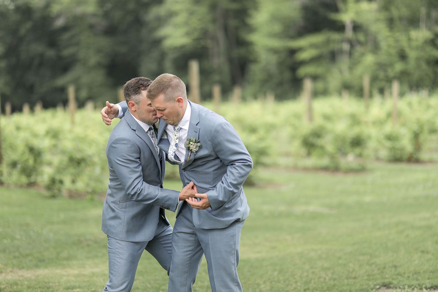 Wedding party in light blue suits pose playfully on lush green grass.