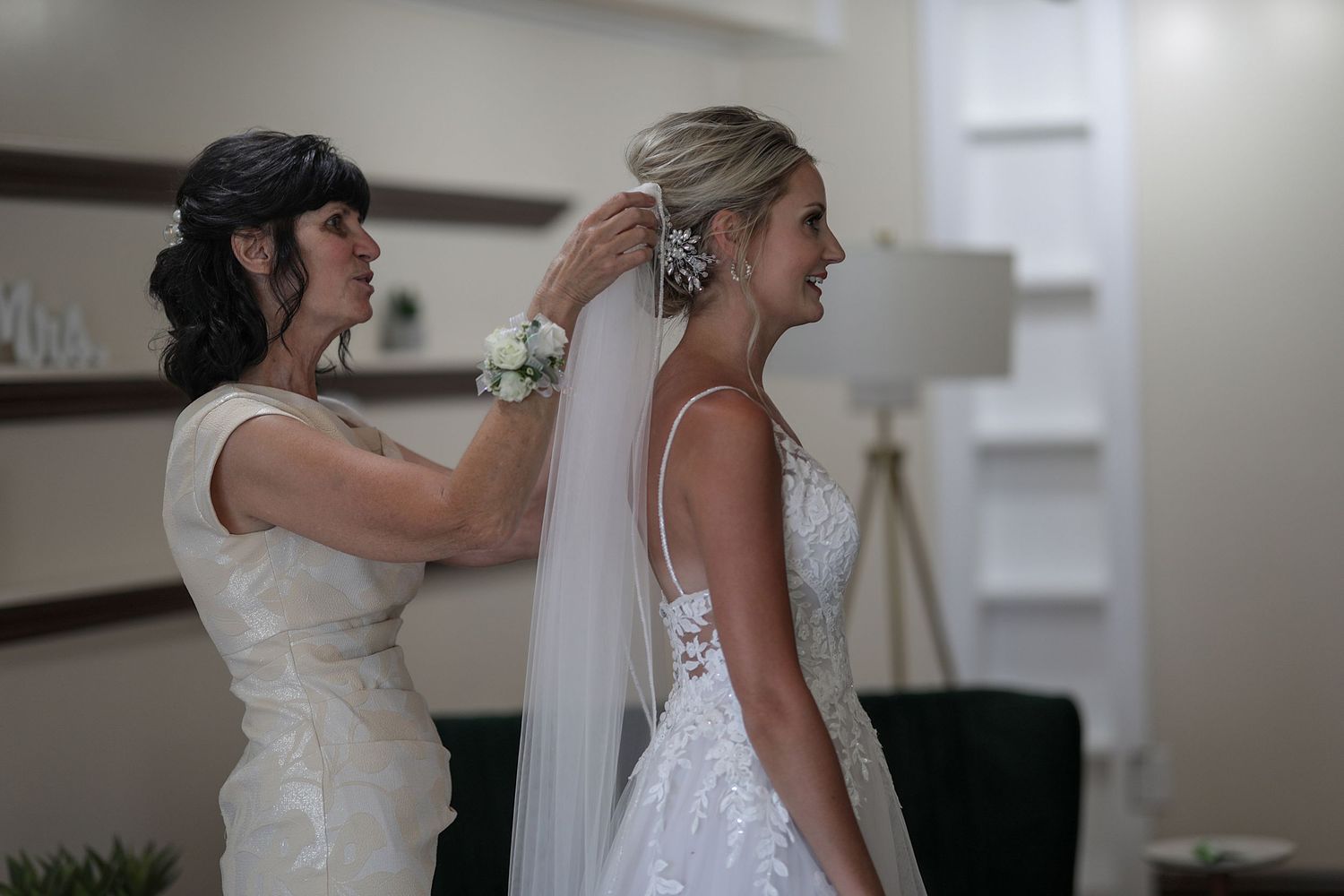 Two women in white dresses help with final preparations during a wedding ceremony.