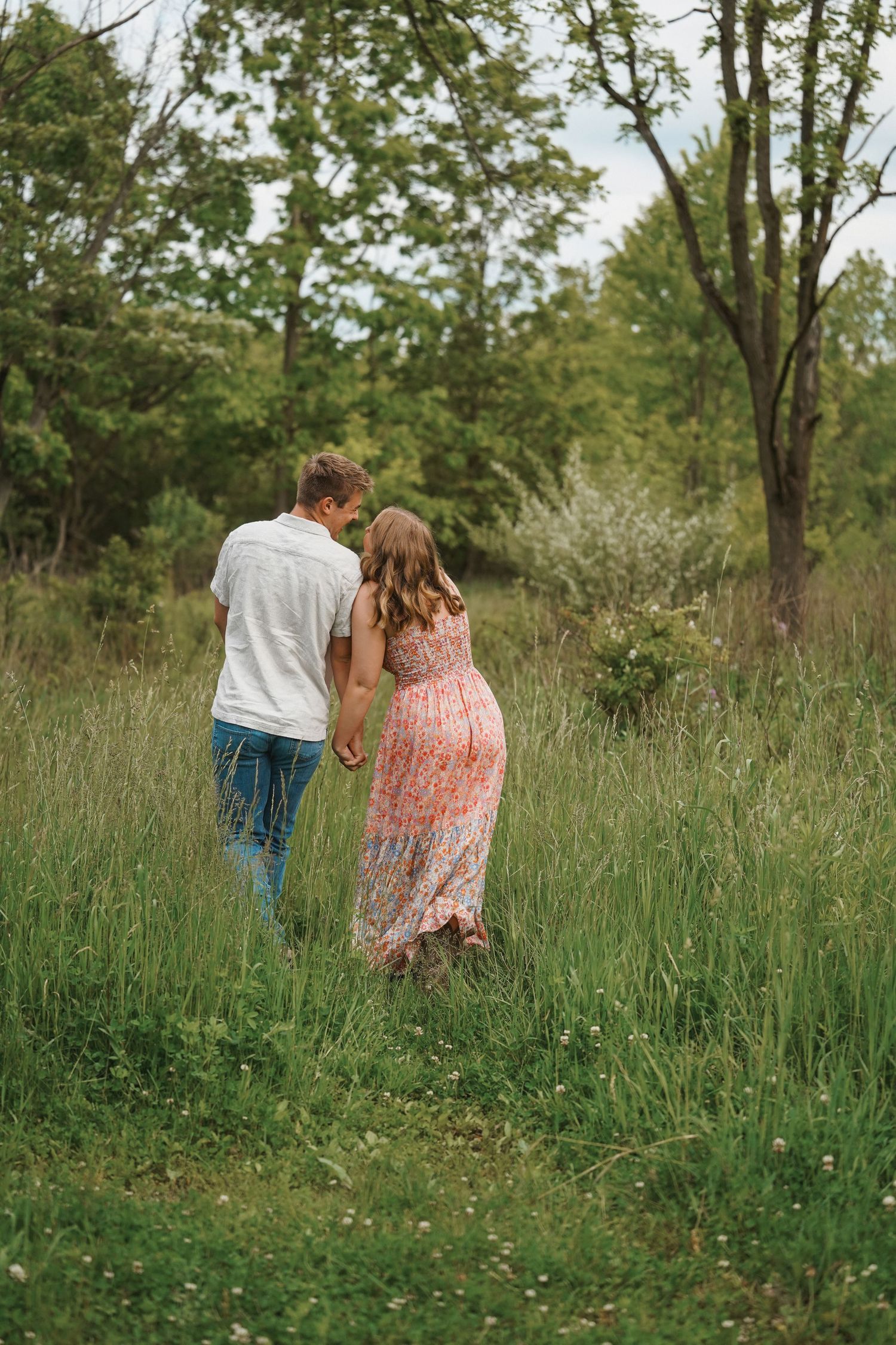 Couple walking together through tall grass and wildflowers in a serene meadow on a sunny afternoon.