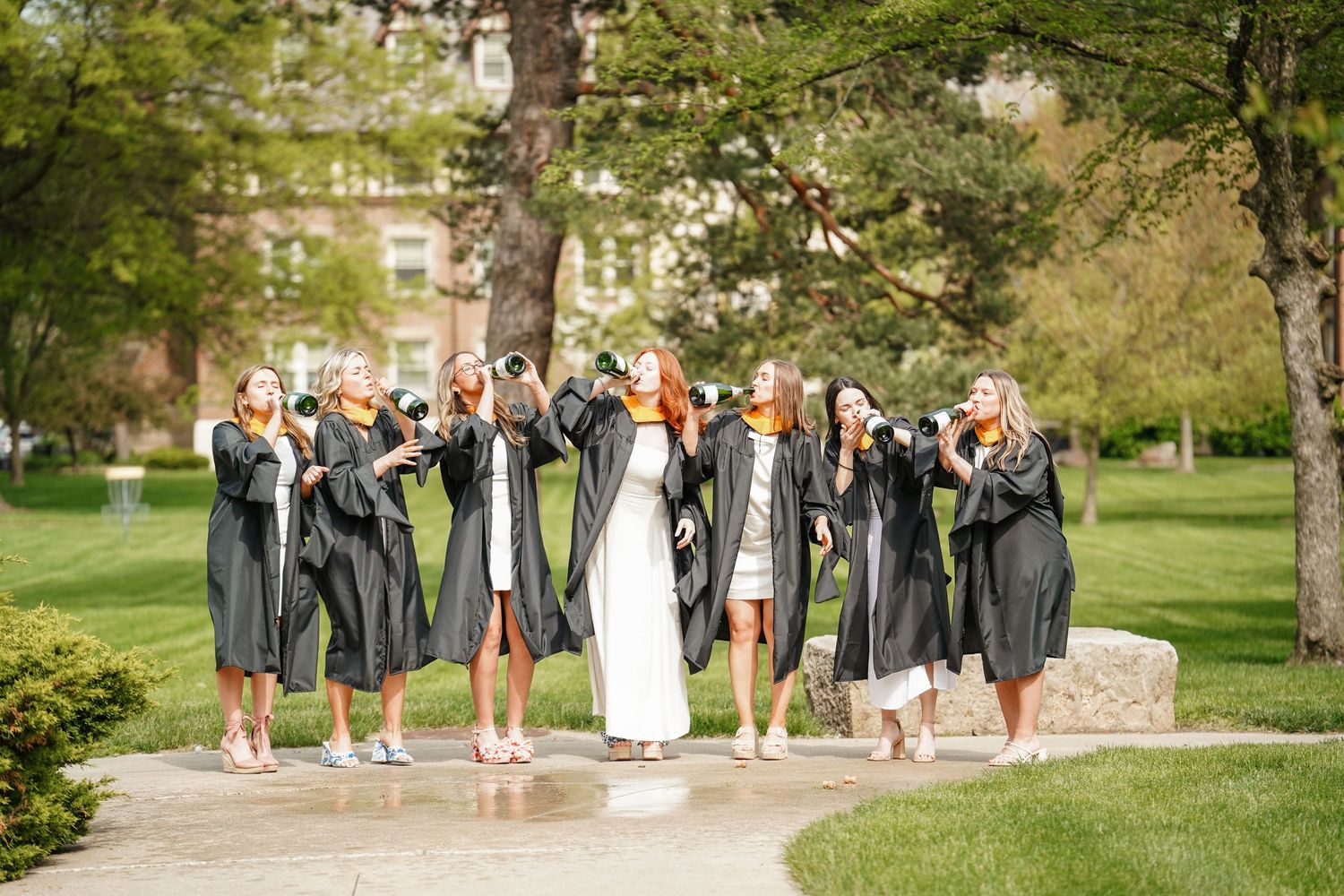 A wedding party stands together on lush green grass during an outdoor summer ceremony.