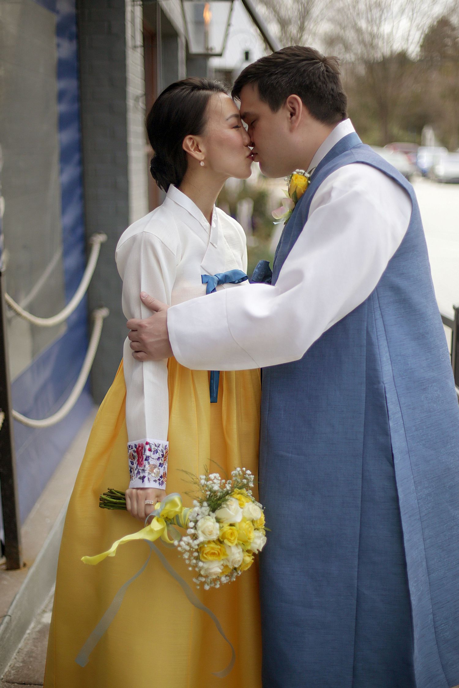 Romantic couple sharing a kiss while dressed in yellow and blue outfits with a spring wedding bouquet.