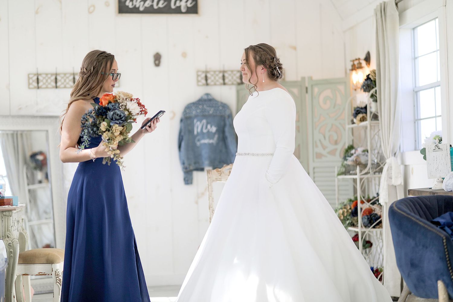 Two people embrace in a bright white room with elegant floral decorations and drapery around them.