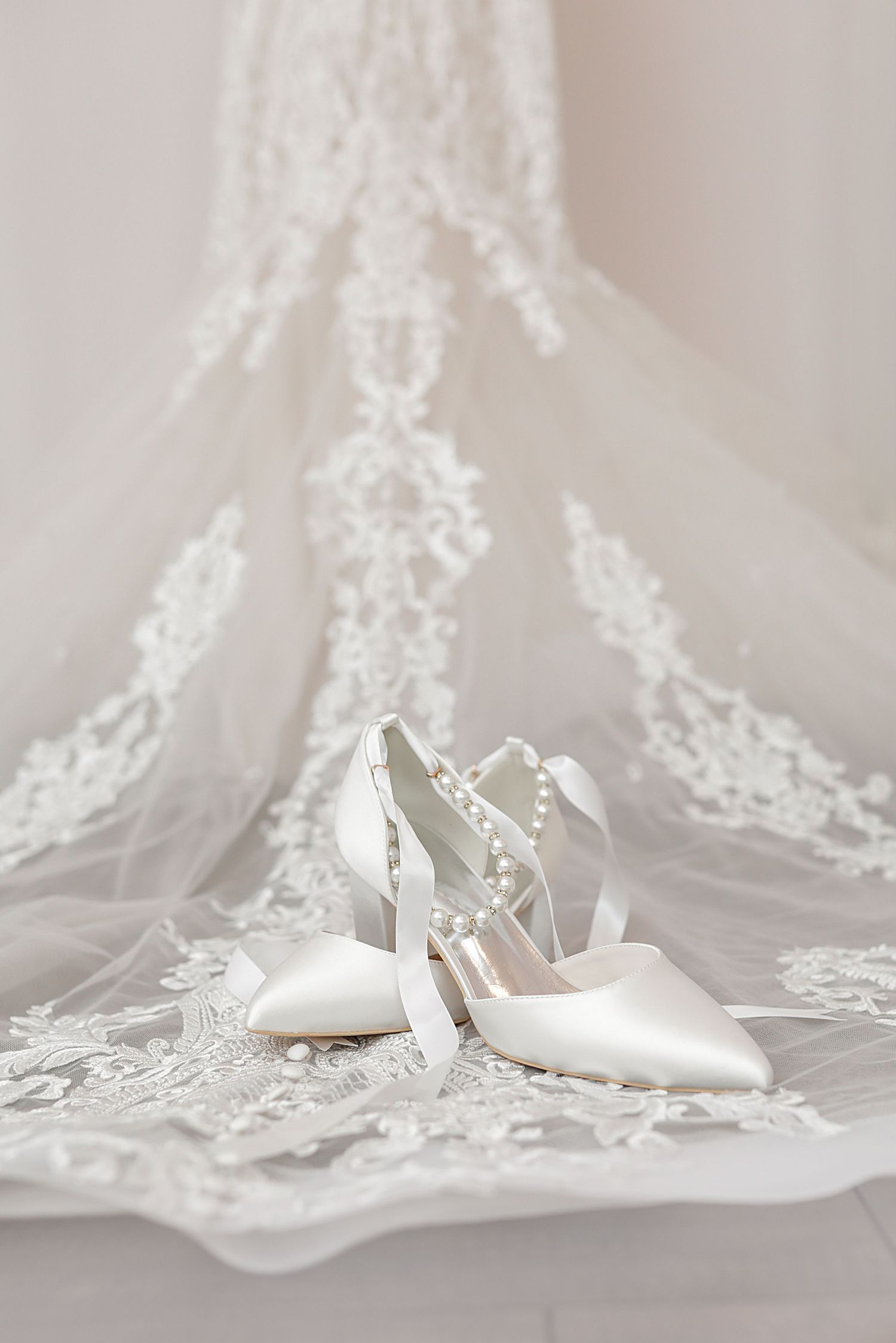Elegant white bridal shoes with pearl details displayed on delicate lace wedding veil. Wedding Photographer in Cleveland Ohio