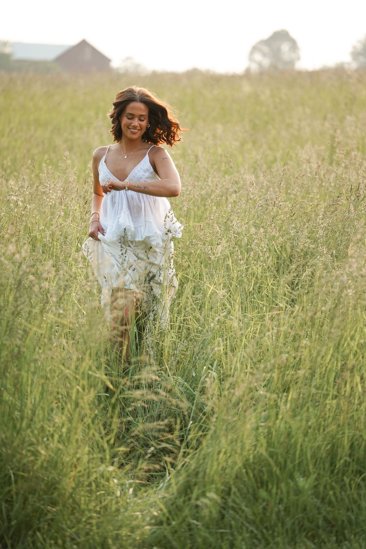 Woman in white dress walking through tall grass field at sunset. Senior Portraits Strongsville Ohio