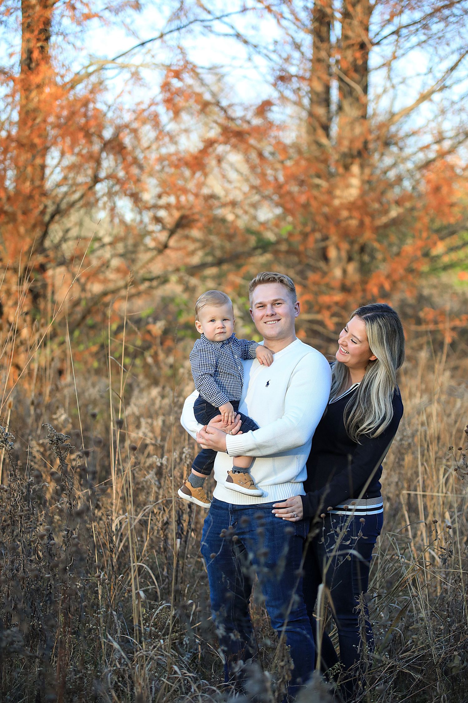 Family portrait in tall autumn grass with warm golden sunlight filtering through trees.  Family Photography in Medina Ohio