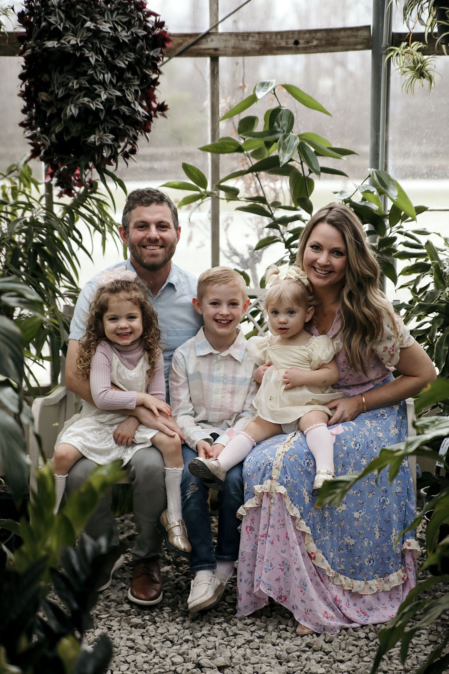 A family poses together in a greenhouse surrounded by lush plants and greenery.