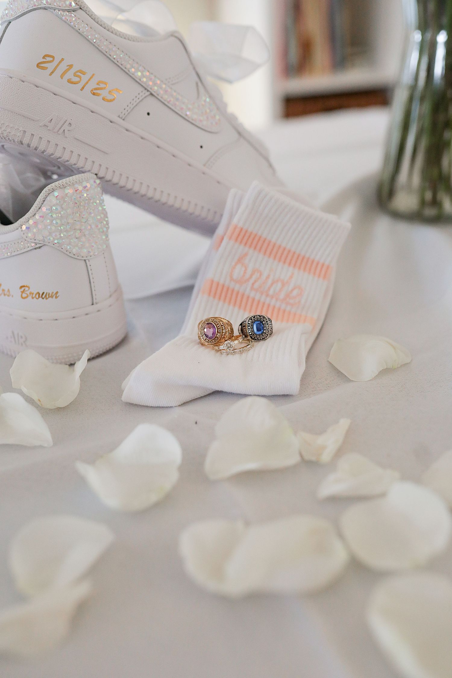 White Nike Air Force 1 sneakers with custom details alongside white socks and scattered rose petals on a light surface.