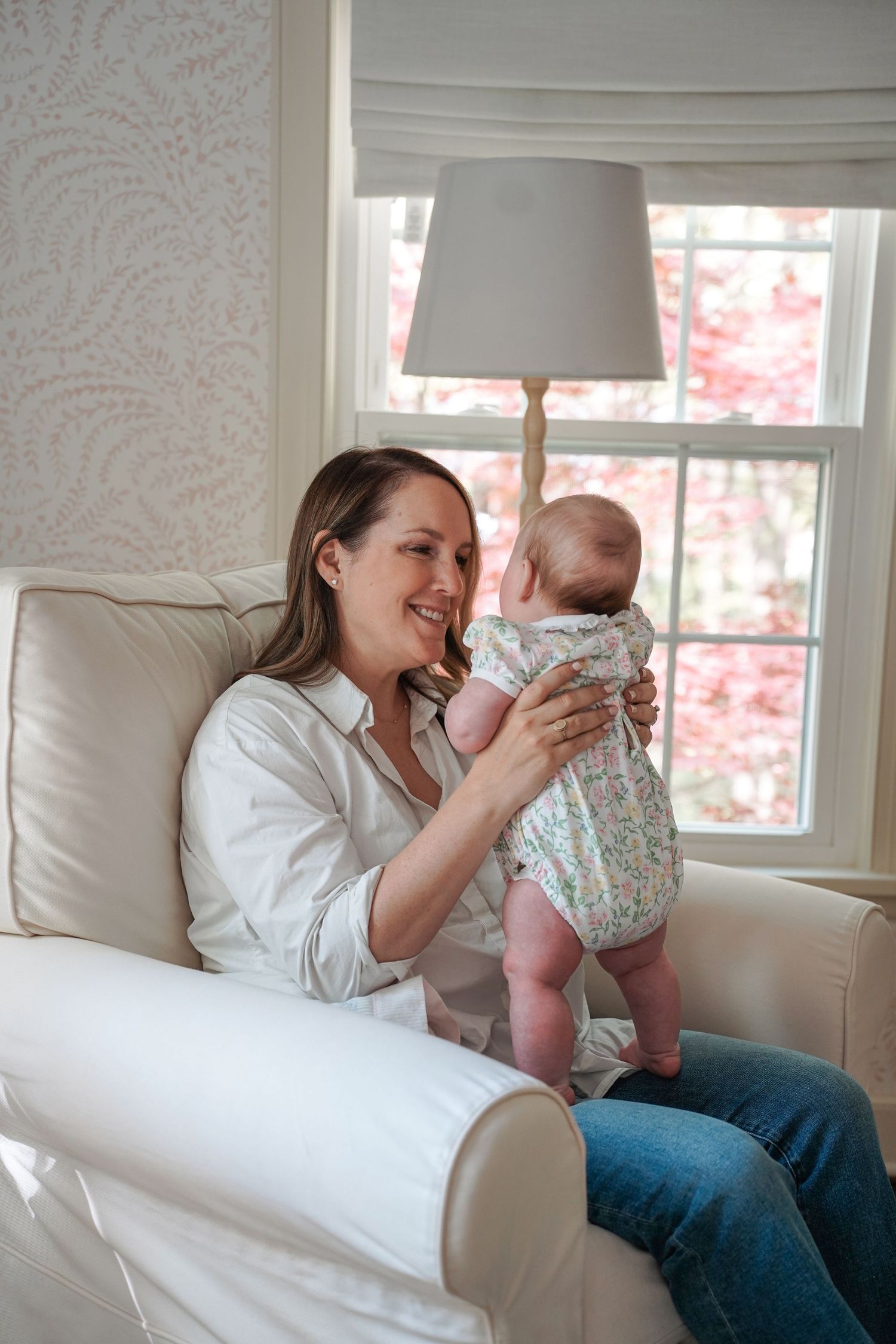 A quiet moment at home as a parent and baby share a tender interaction while sitting in a white armchair by the window.