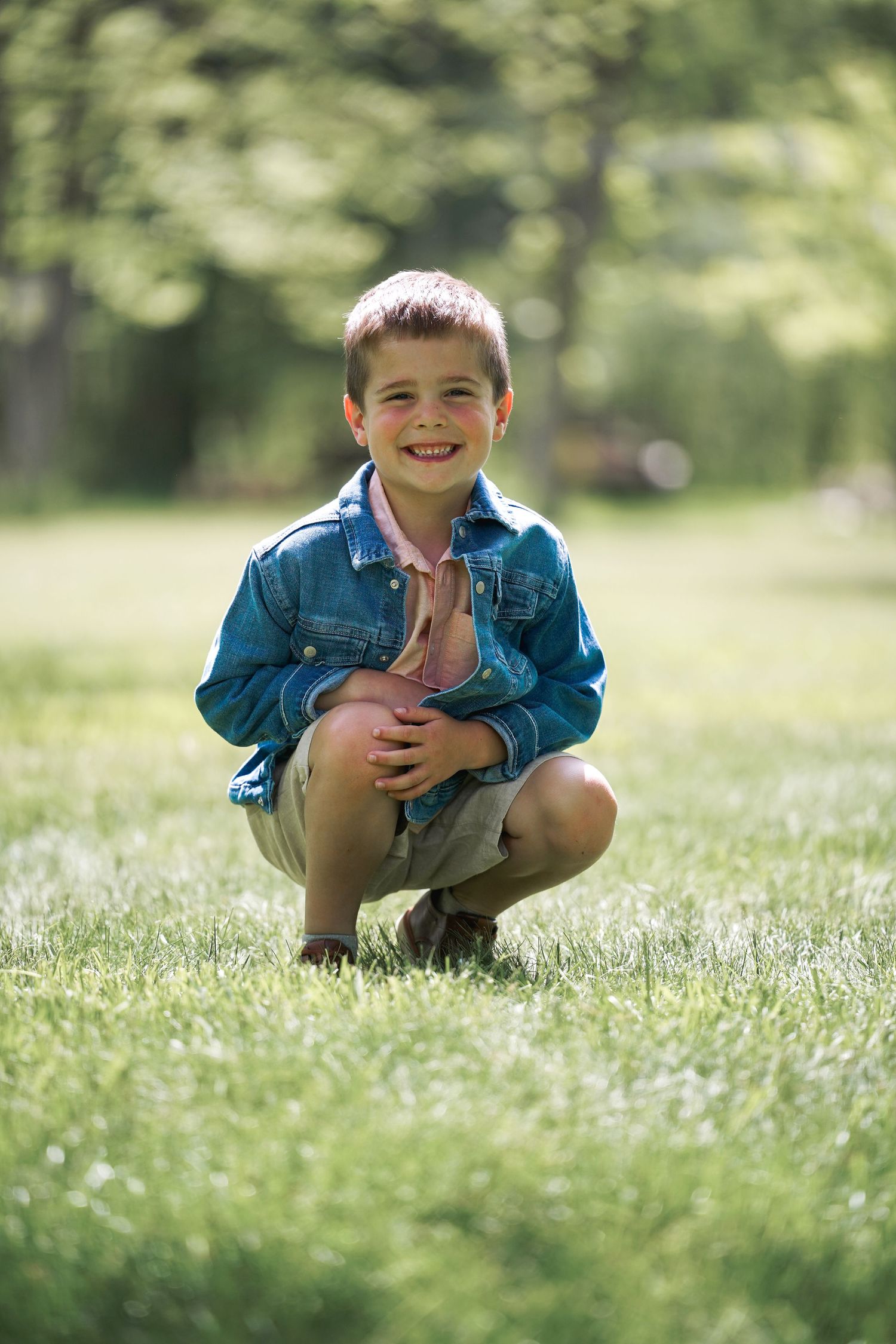 A sequence showing a young child in denim clothes crouching in a sunny grassy field with a playful expression.
