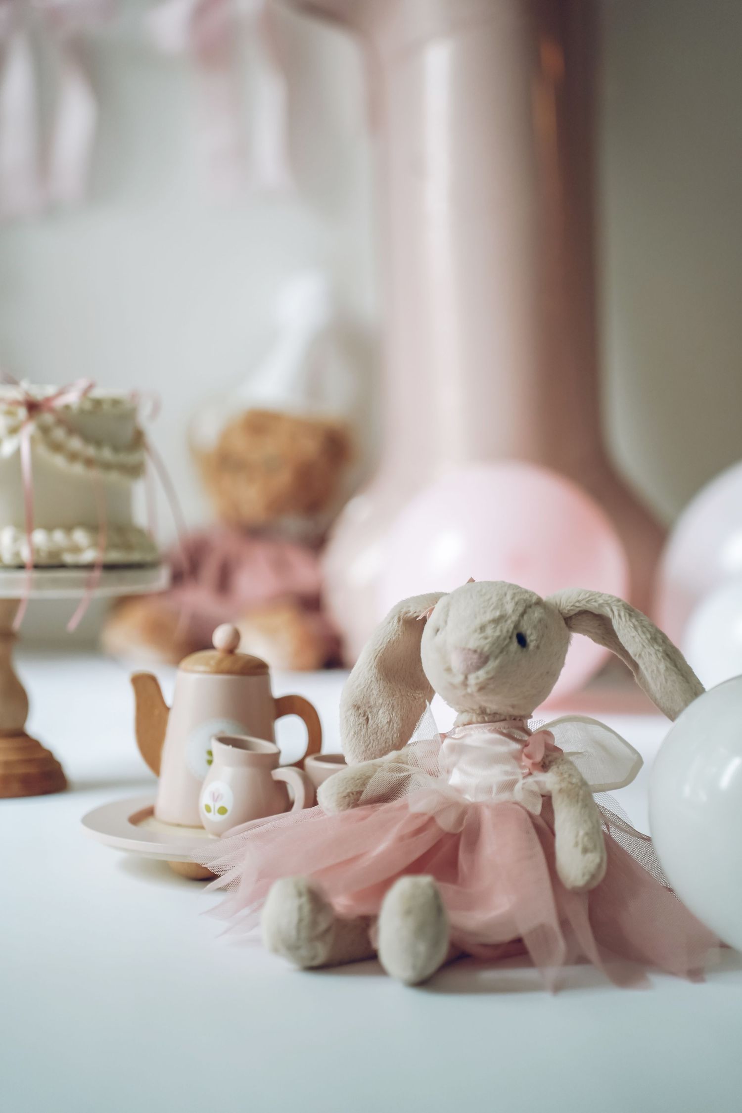 A soft triptych of plush toys adorned with pink ribbons arranged on a white surface in dreamy ethereal composition.