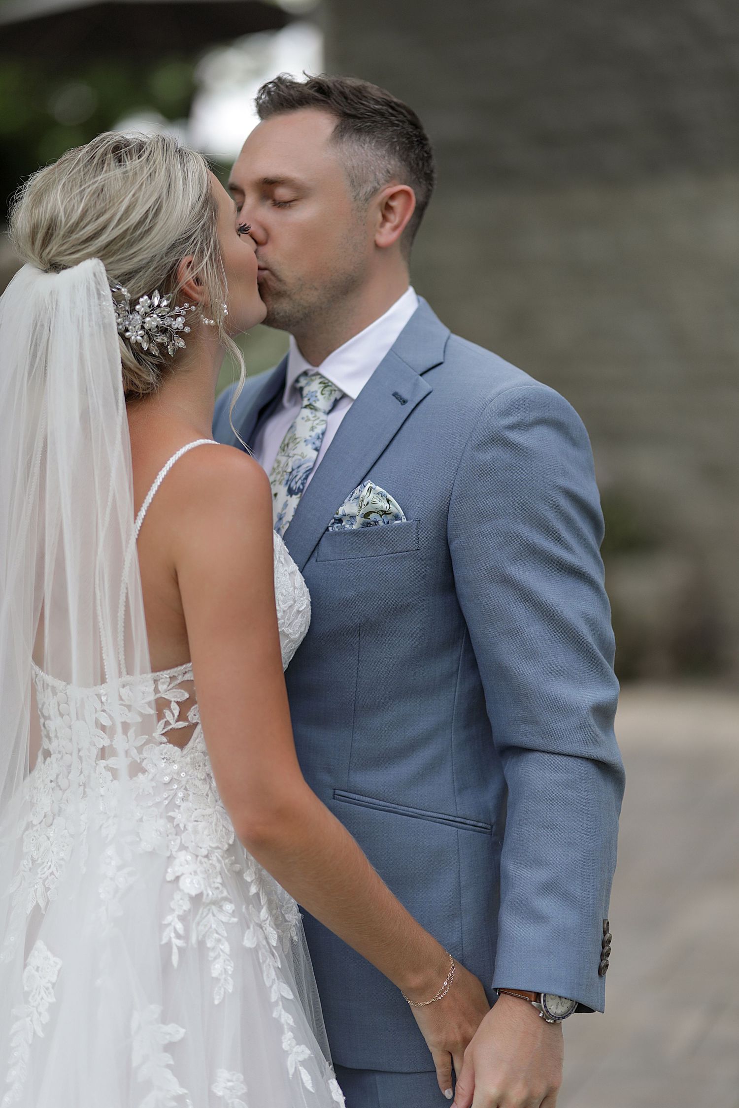 A romantic wedding moment captured with a couple sharing a kiss, showcasing a gray suit and lace bridal gown.