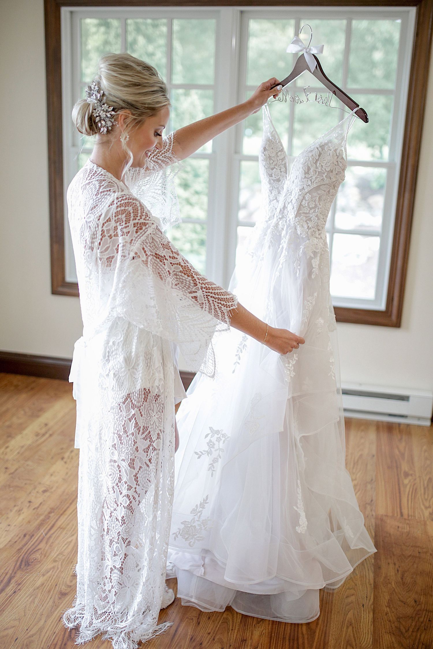 A person in a white lace robe holding up an elegant white wedding dress near a window. Wedding Photographer in Cleveland Ohio