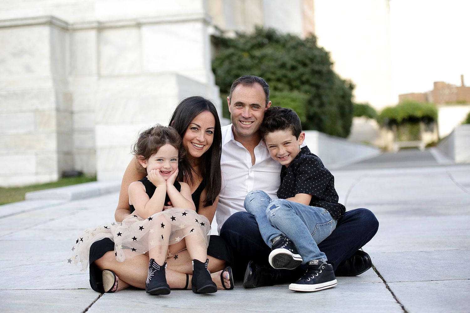 Family of four sitting together and smiling on concrete steps during an outdoor photo session.  Family Photography in Cleveland Ohio