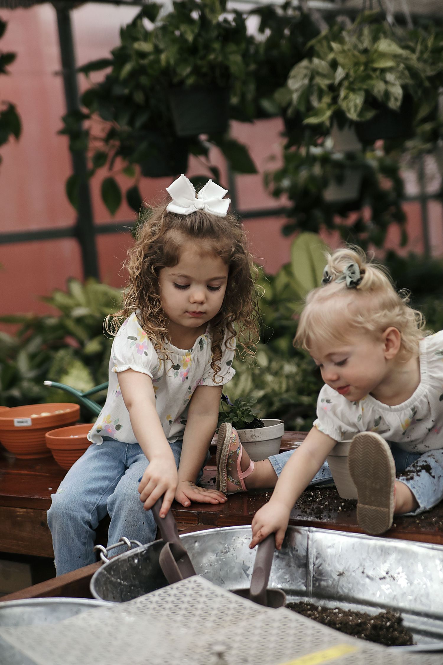 Two children in casual clothes playing together with soil and gardening materials in an outdoor setting.