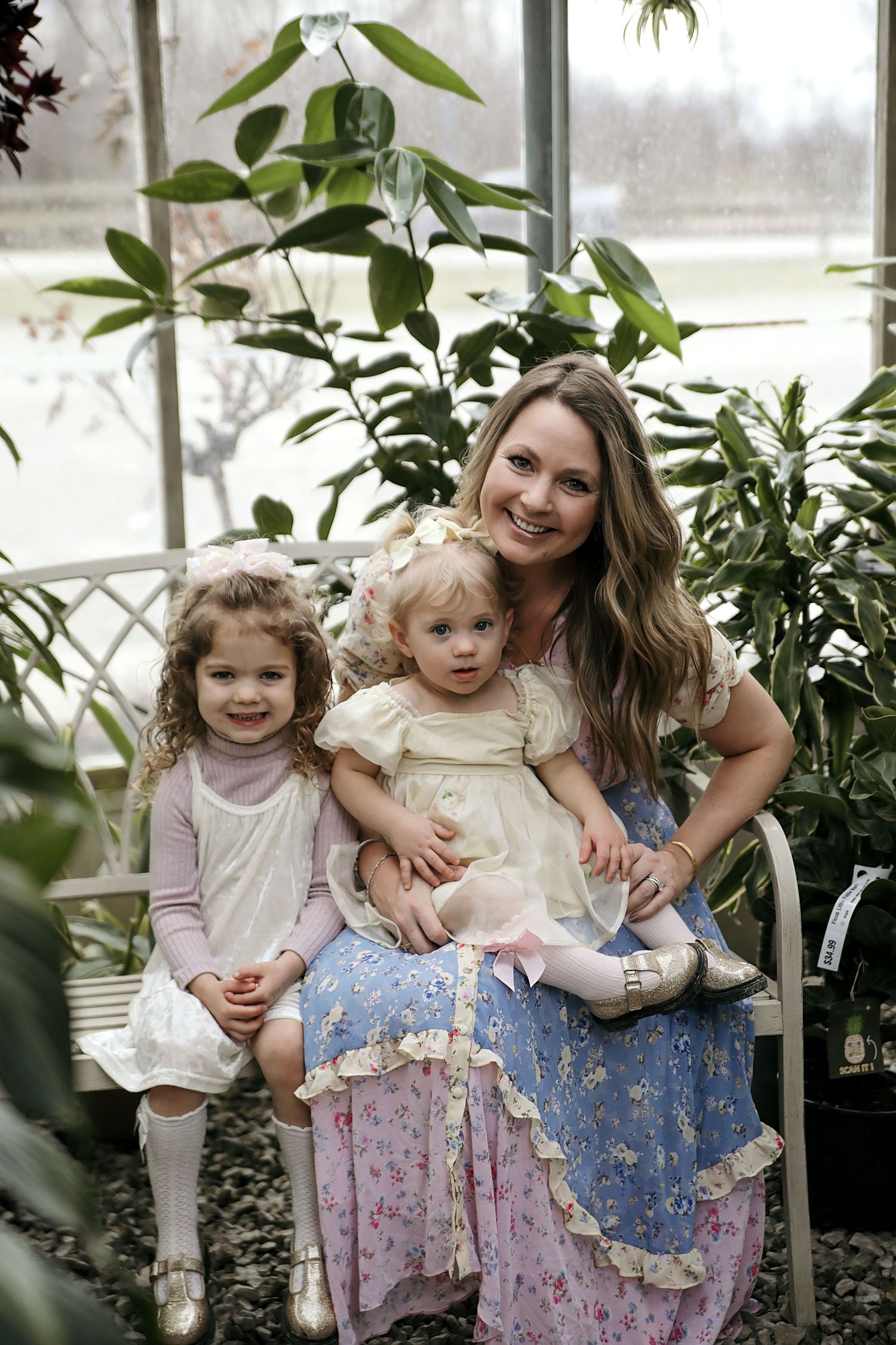 Family portrait series in a lush greenhouse with matching floral dresses surrounded by green plants.