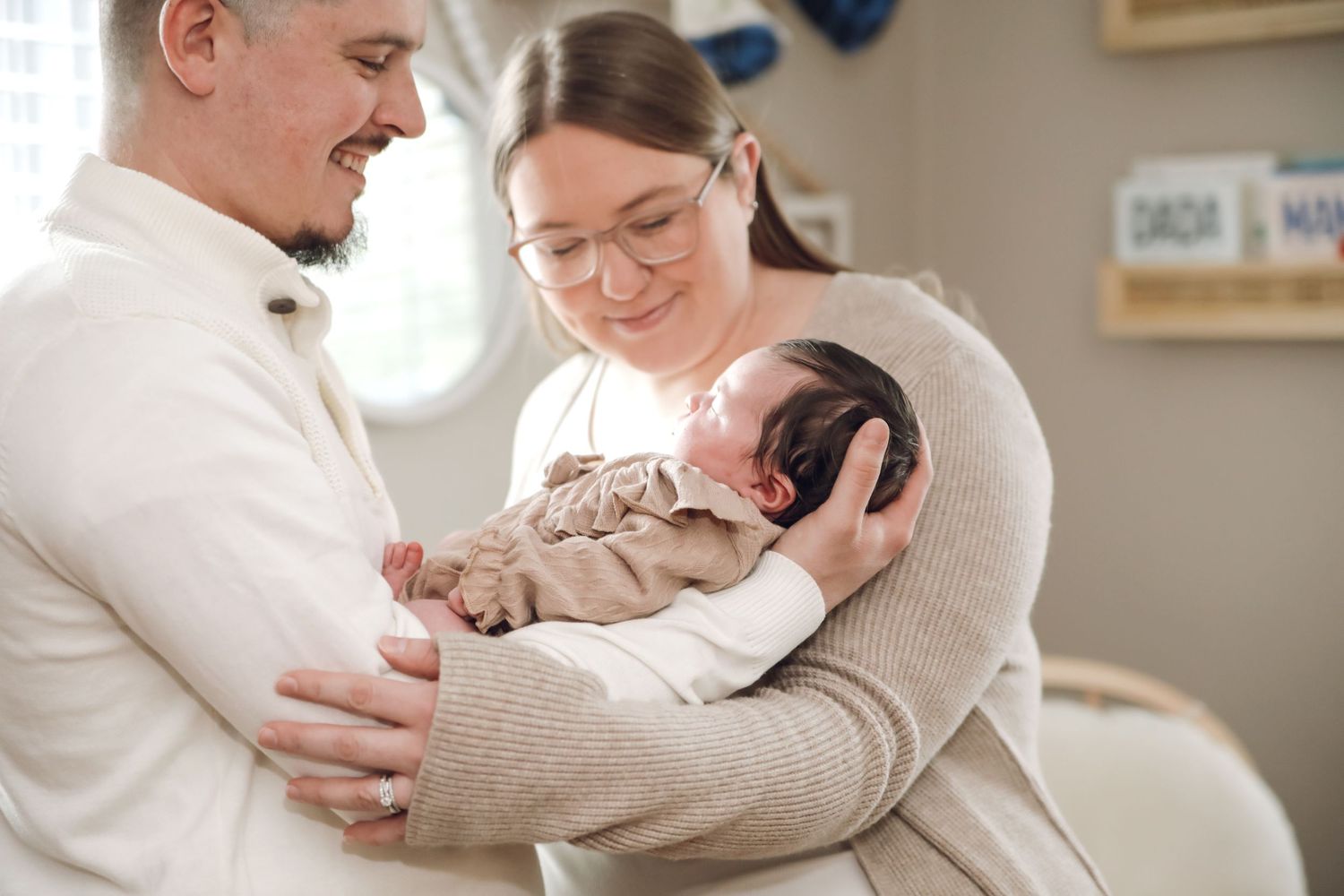A person in a beige sweater holds and cuddles with a small white puppy in a bright interior setting.
