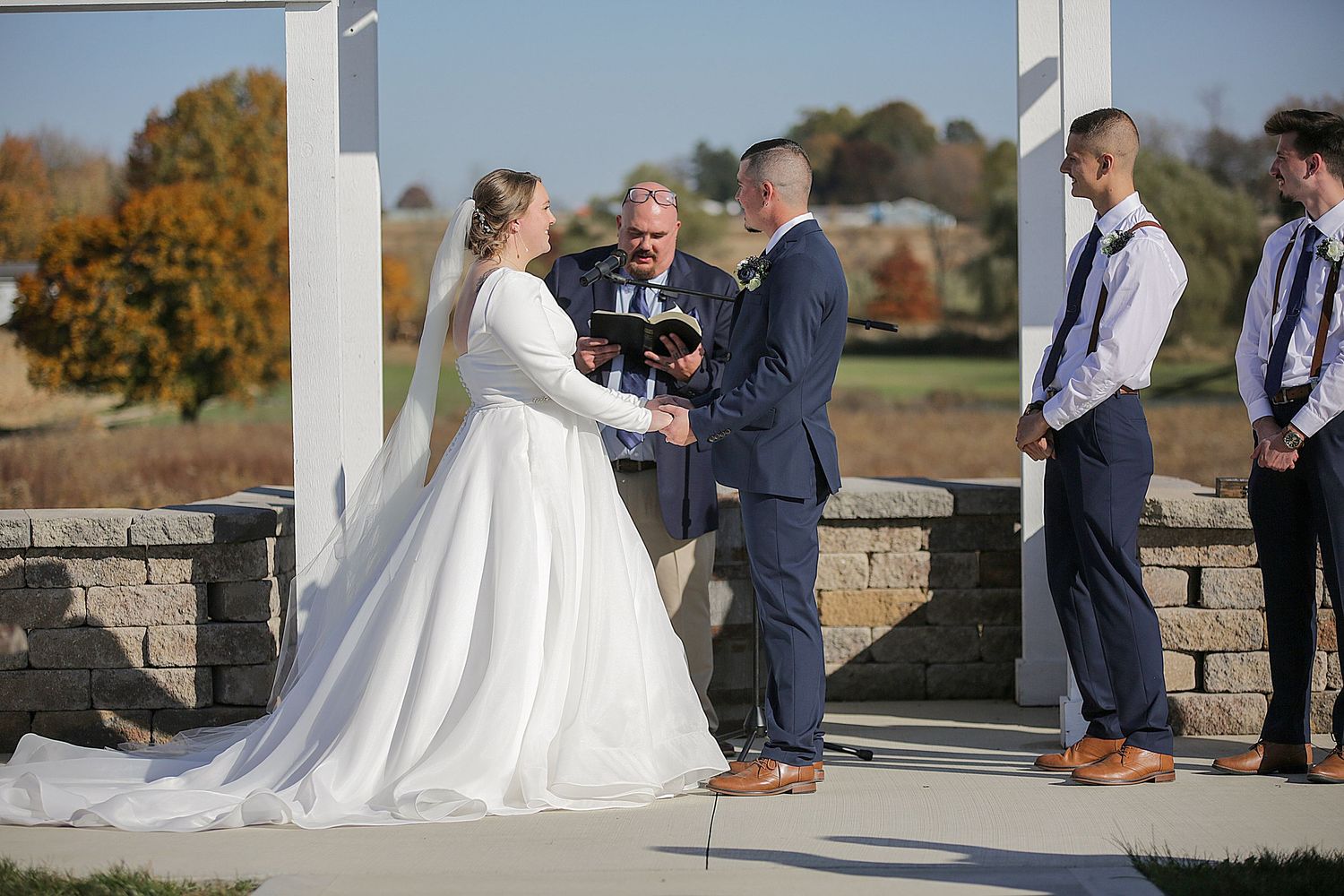 An outdoor wedding ceremony being conducted on a stone platform with groomsmen in attendance.