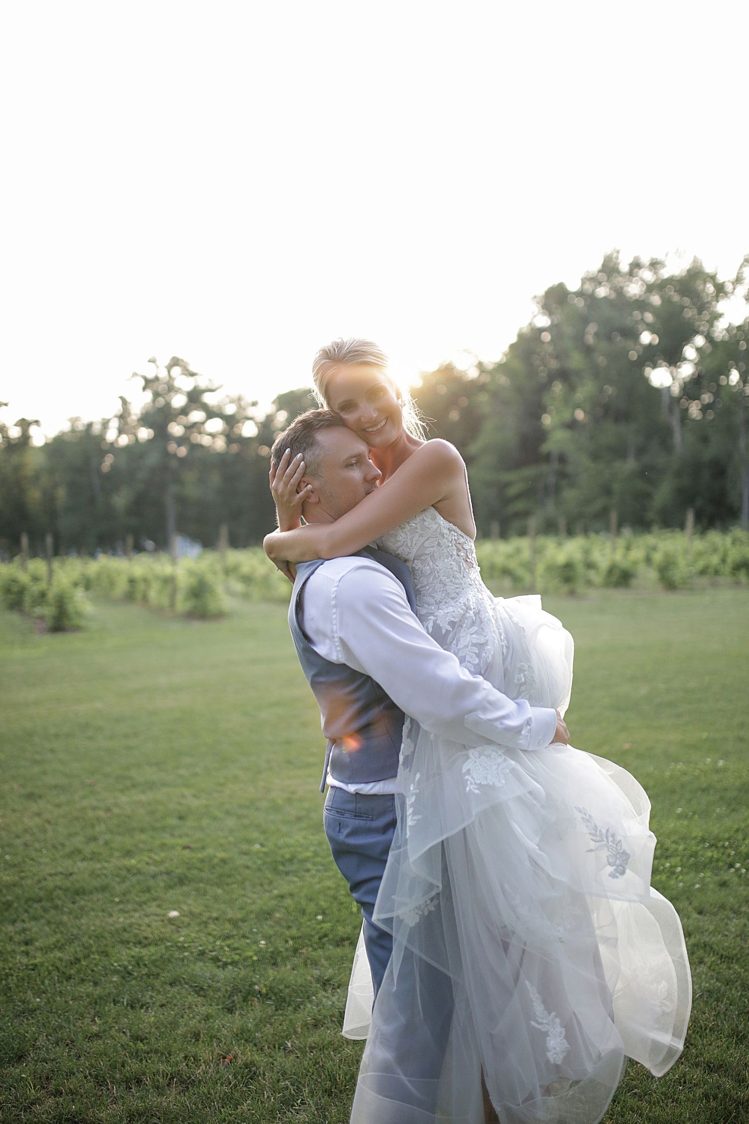 Romantic sunset wedding portrait with couple embracing in open field.