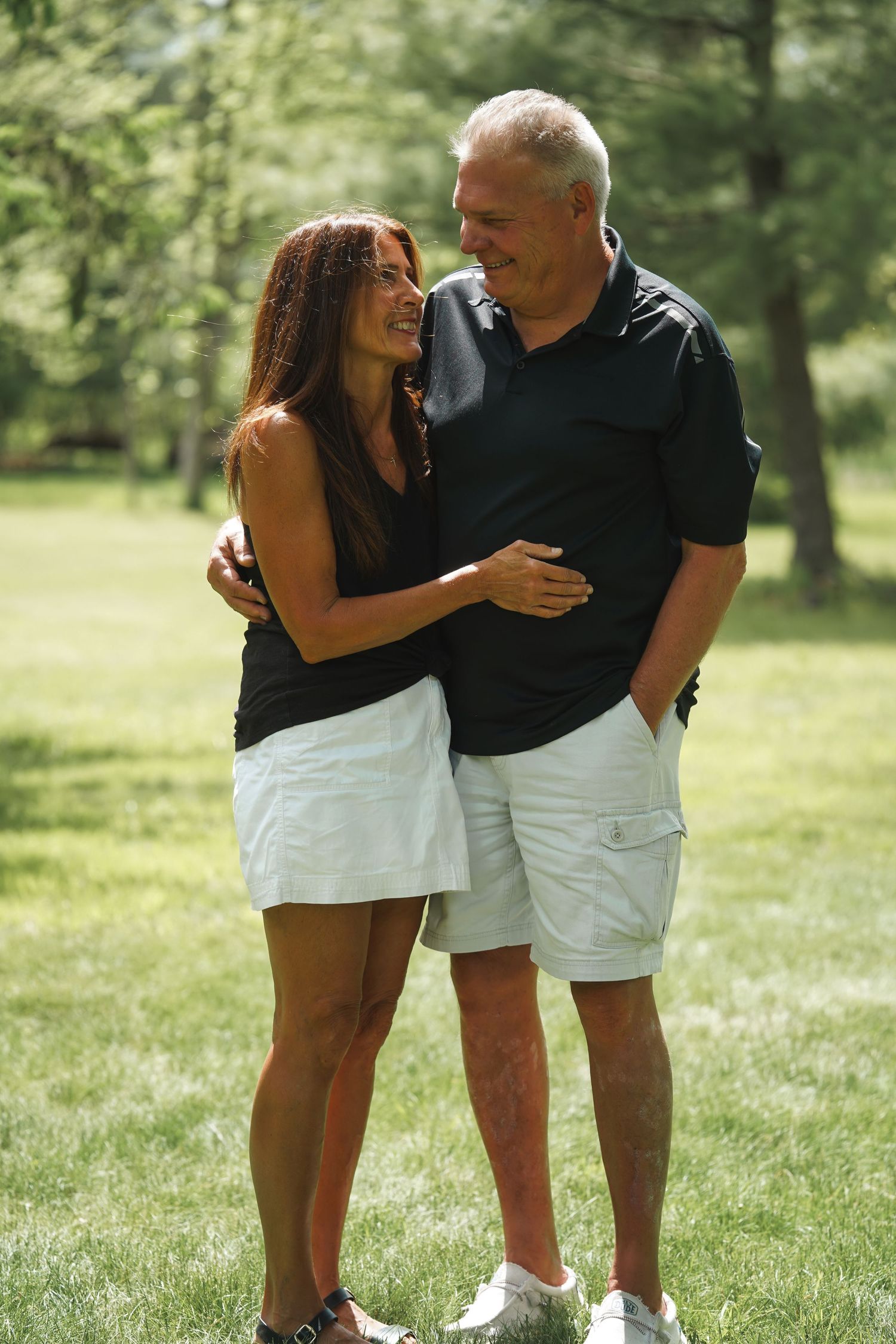 A romantic couple wearing black and white outfits share a tender moment while embracing on a sunny lawn.