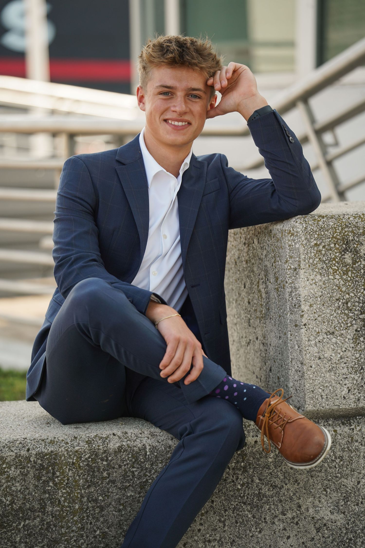Young professional in navy suit reclines on concrete steps while wearing brown leather dress shoes and white shirt.