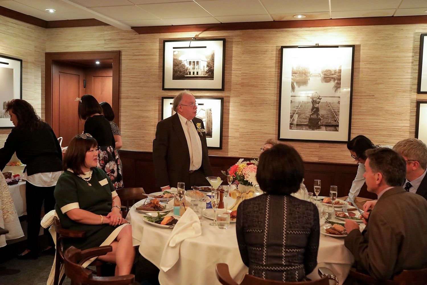 Diners enjoy a meal at an upscale restaurant with wood paneled walls and framed artwork.