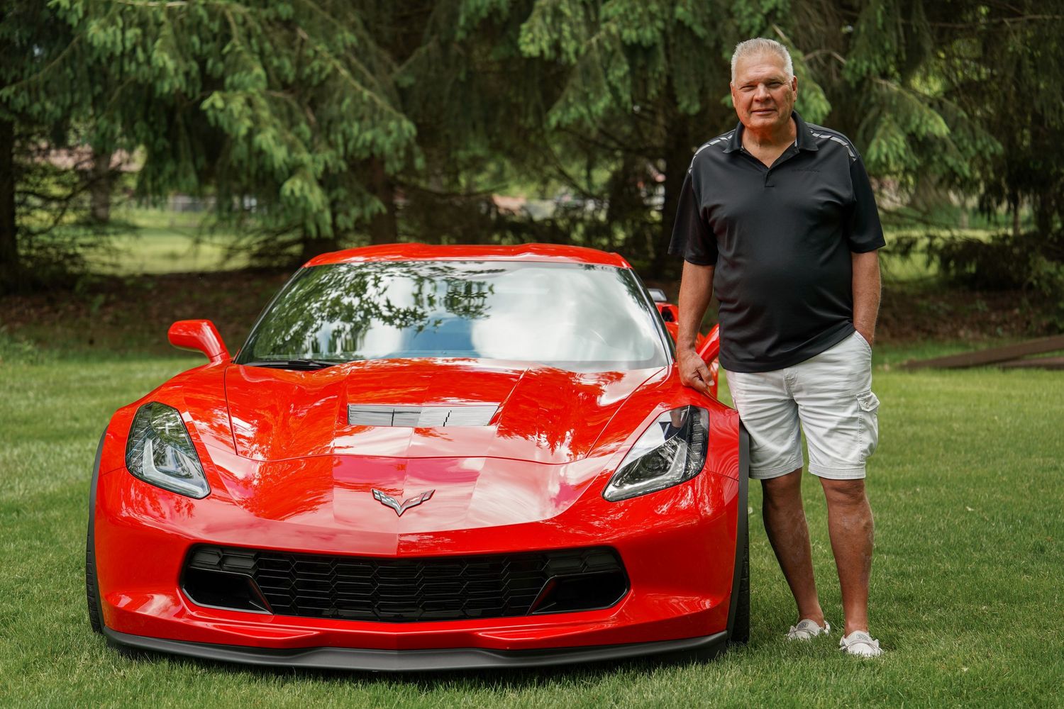 A bright red Chevrolet Corvette sits parked on grass near trees, shown from multiple angles in nature.
