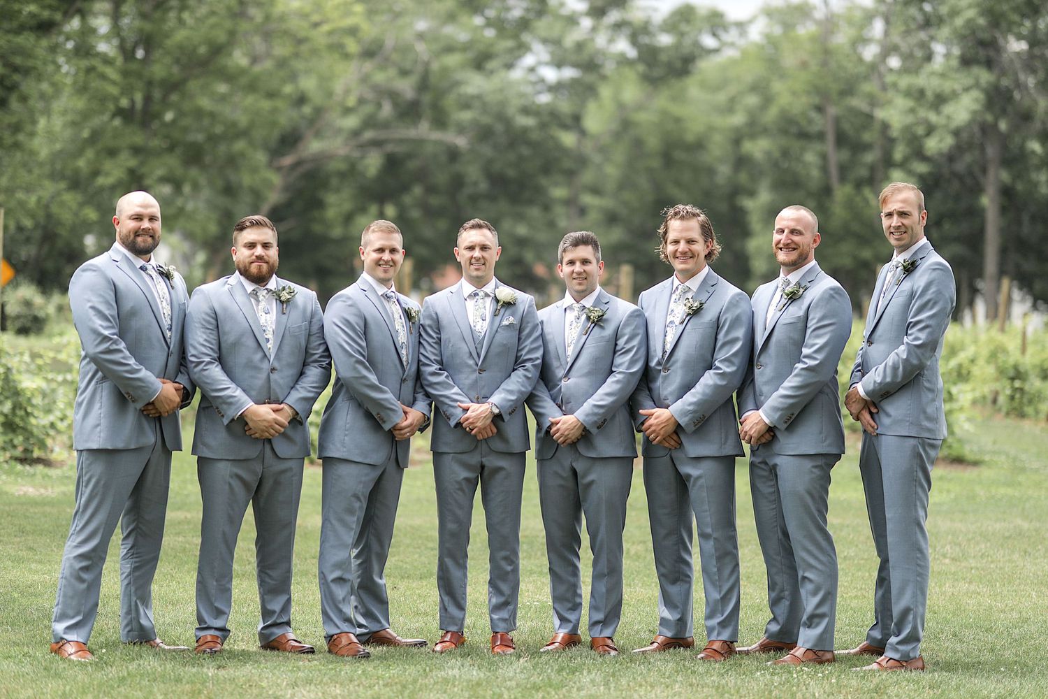 Groomsmen in matching gray suits lined up for a fun photo on grass.