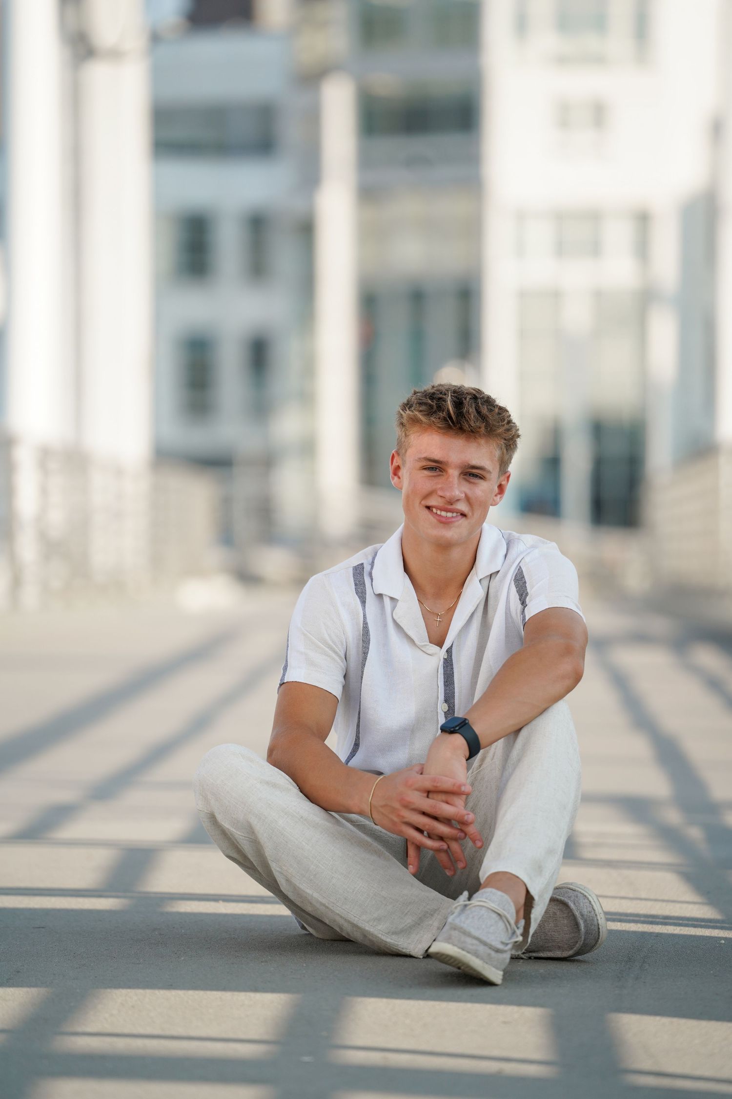 Young person in white shirt lounges casually on sunny floor with bright modern architecture in background.