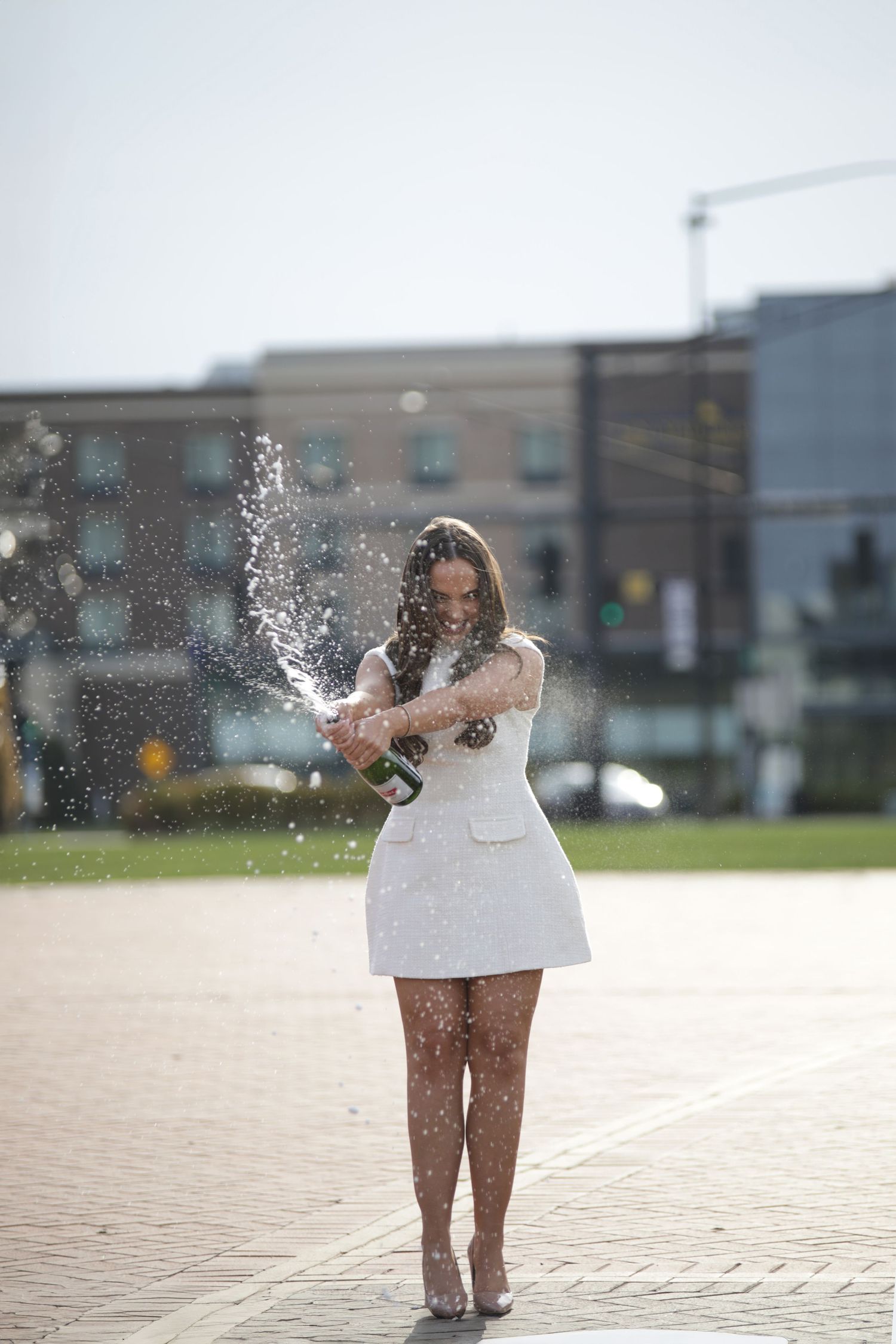 A person in a white dress stands in a sunlit plaza with water droplets splashing around them in a sequence of photos.