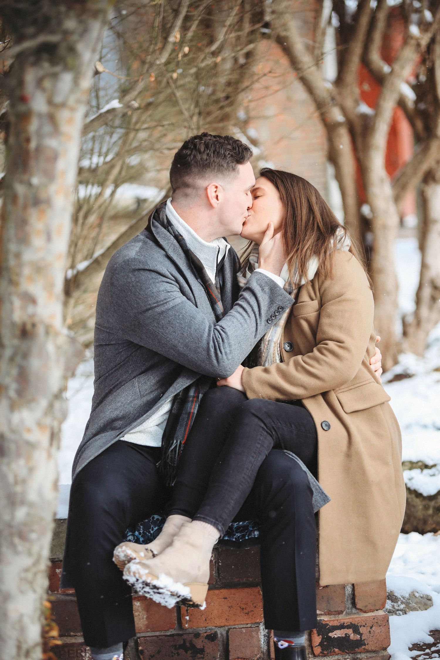 A romantic winter scene with a couple sharing a tender kiss while sitting on vintage luggage in a snowy forest.